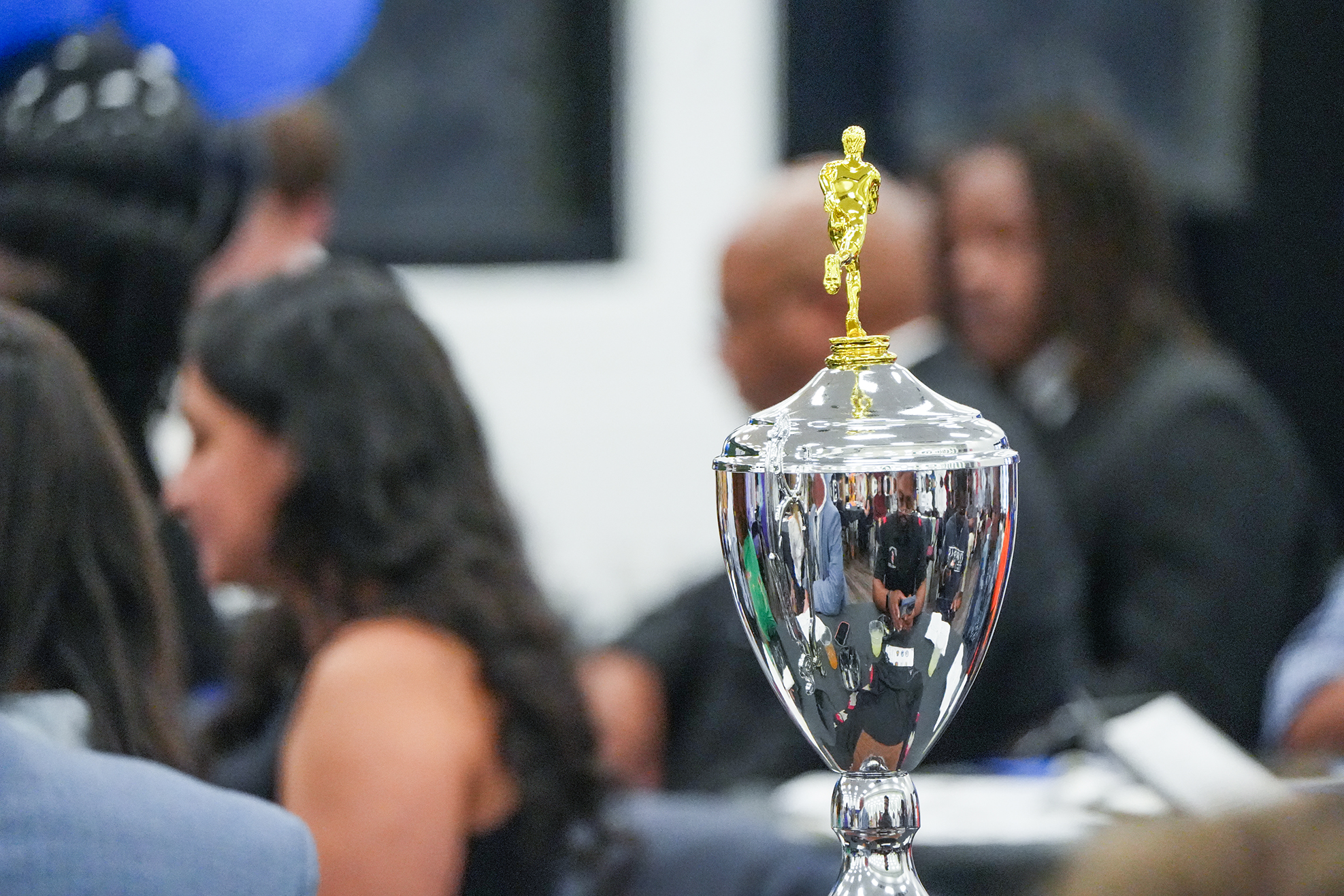Silver trophy with golden Oscar figure on top, surrounded by people sitting at a table.