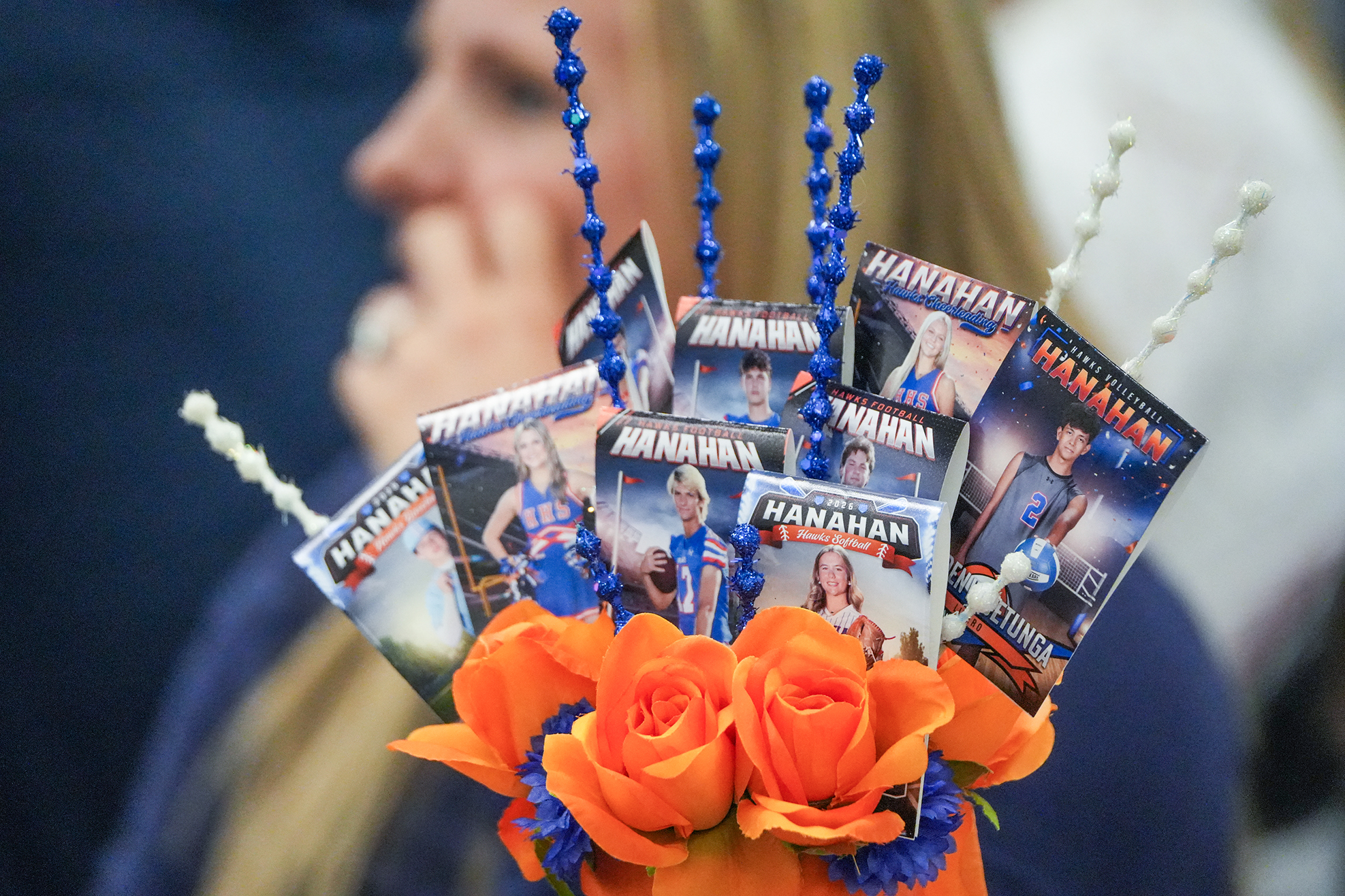A bouquet of roses and small cards with photos and names displayed in an orange vase.