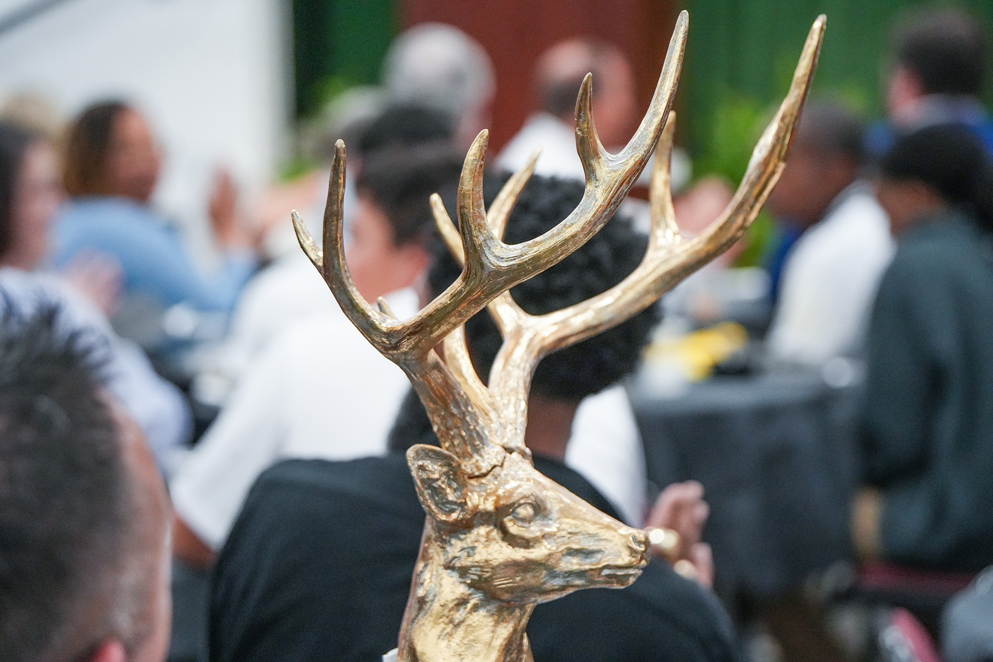People seated around a table, a blurry gold deer head decoration in the foreground.