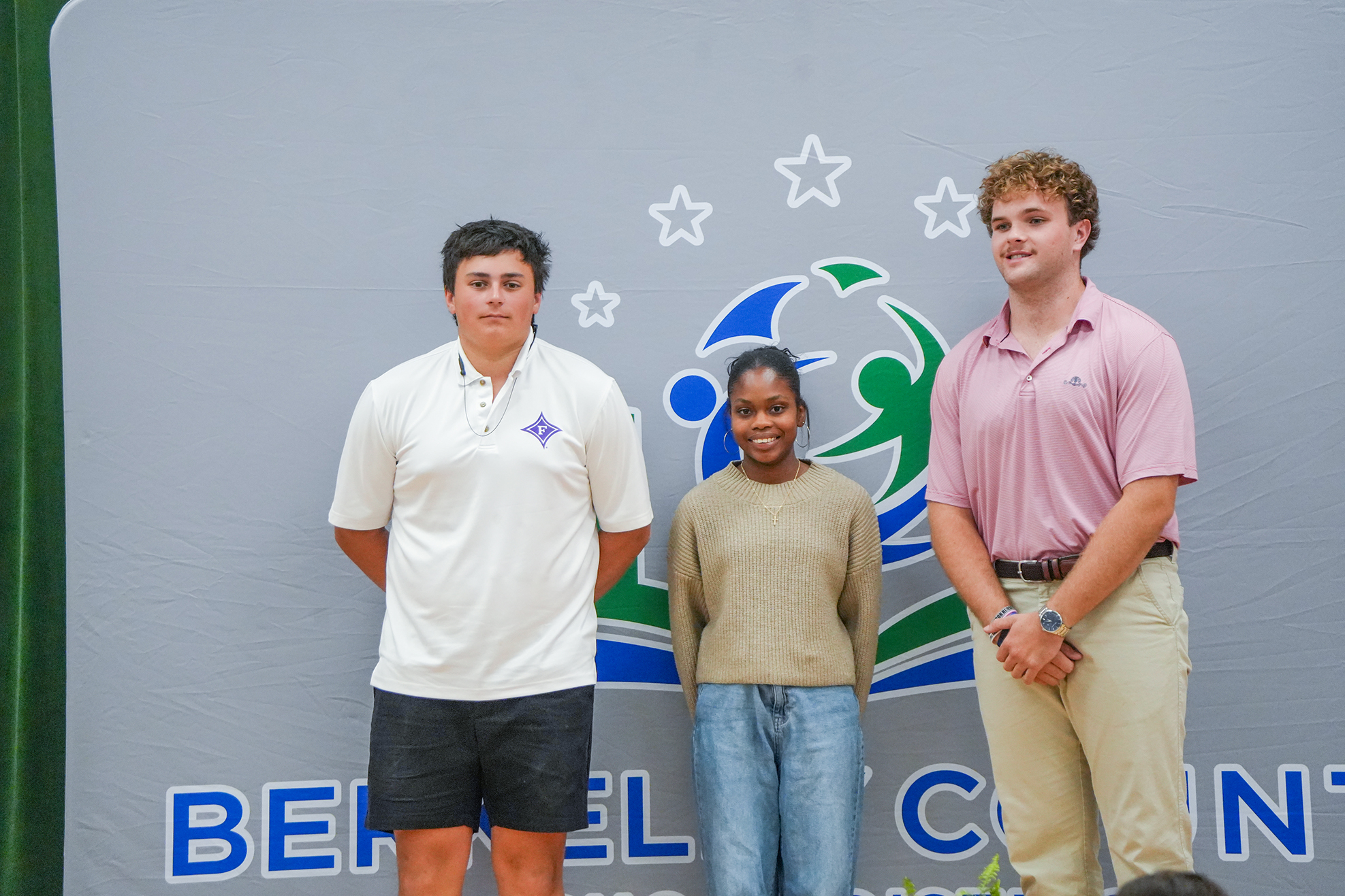 Three individuals stand together on a stage with a backdrop that reads "Beh El Count".
