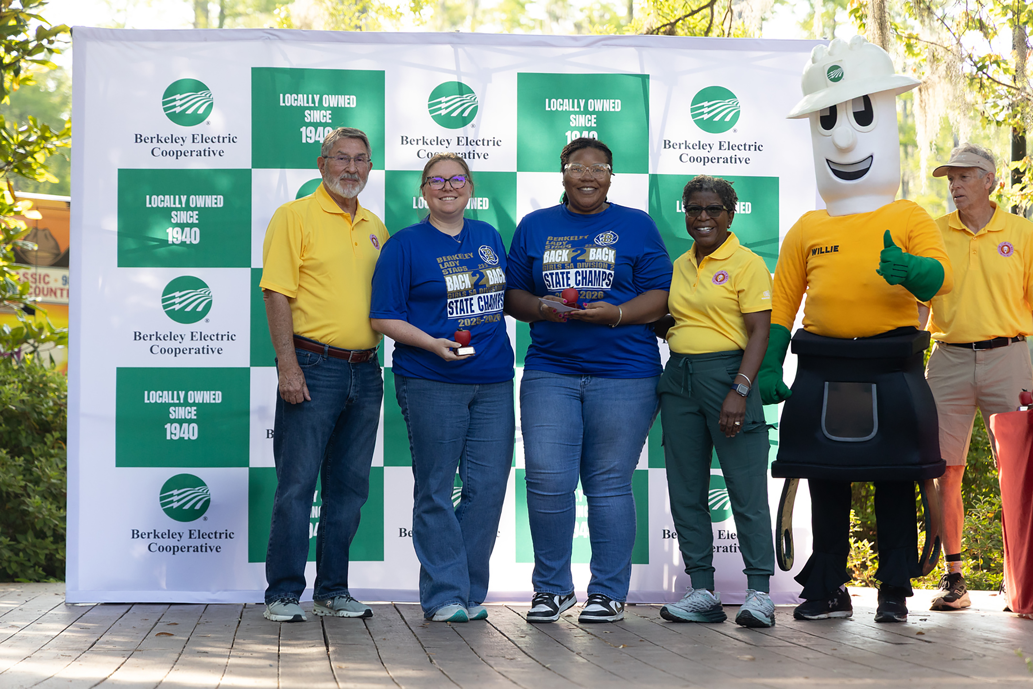 Five people pose for a photo, holding awards. Two wear blue, two wear yellow, and one is a mascot.