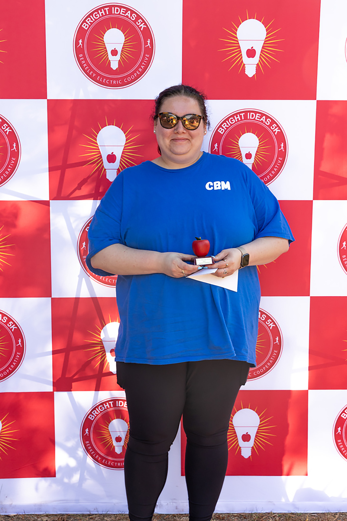 Person with a blue shirt holding an apple in front of a red and white banner.