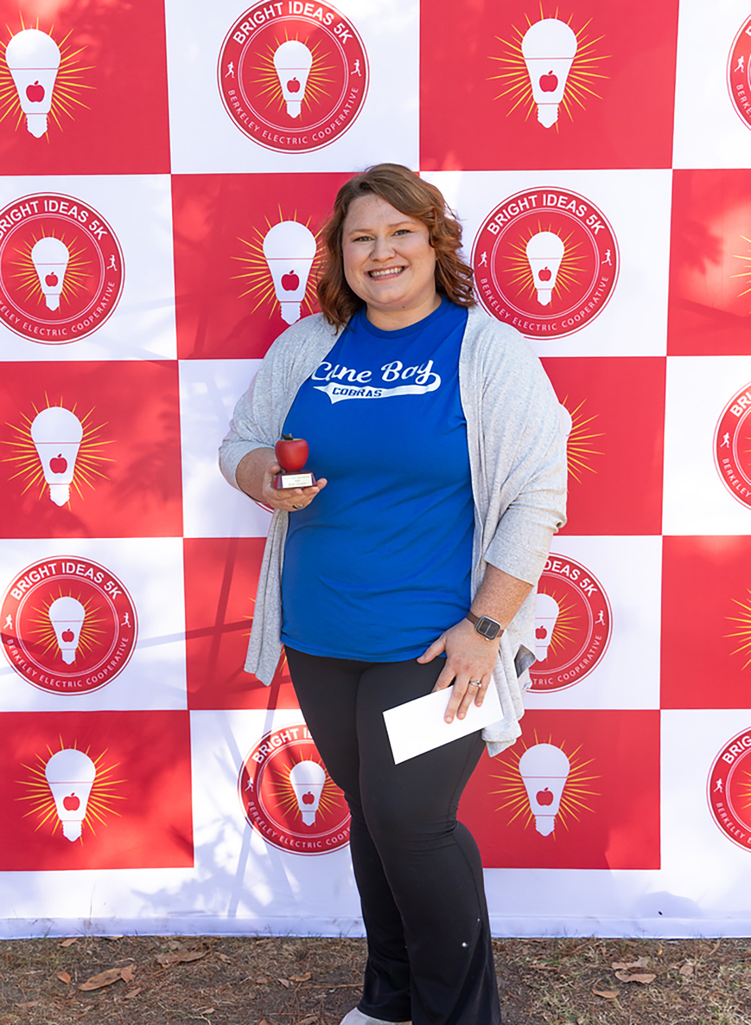Person with an award stands in front of a backdrop with red and white squares and light bulb logos.