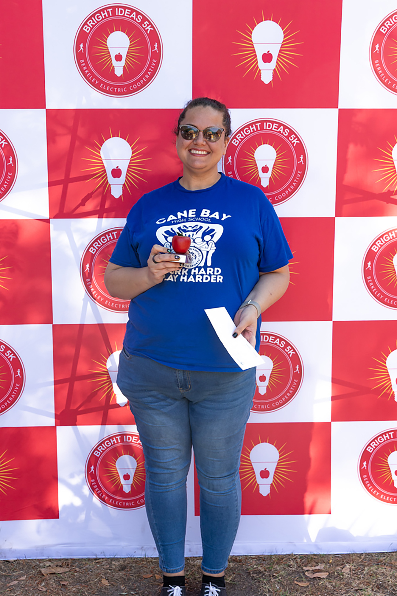 A woman wearing a blue shirt stands before a red and white checkered wall with light bulb logos.