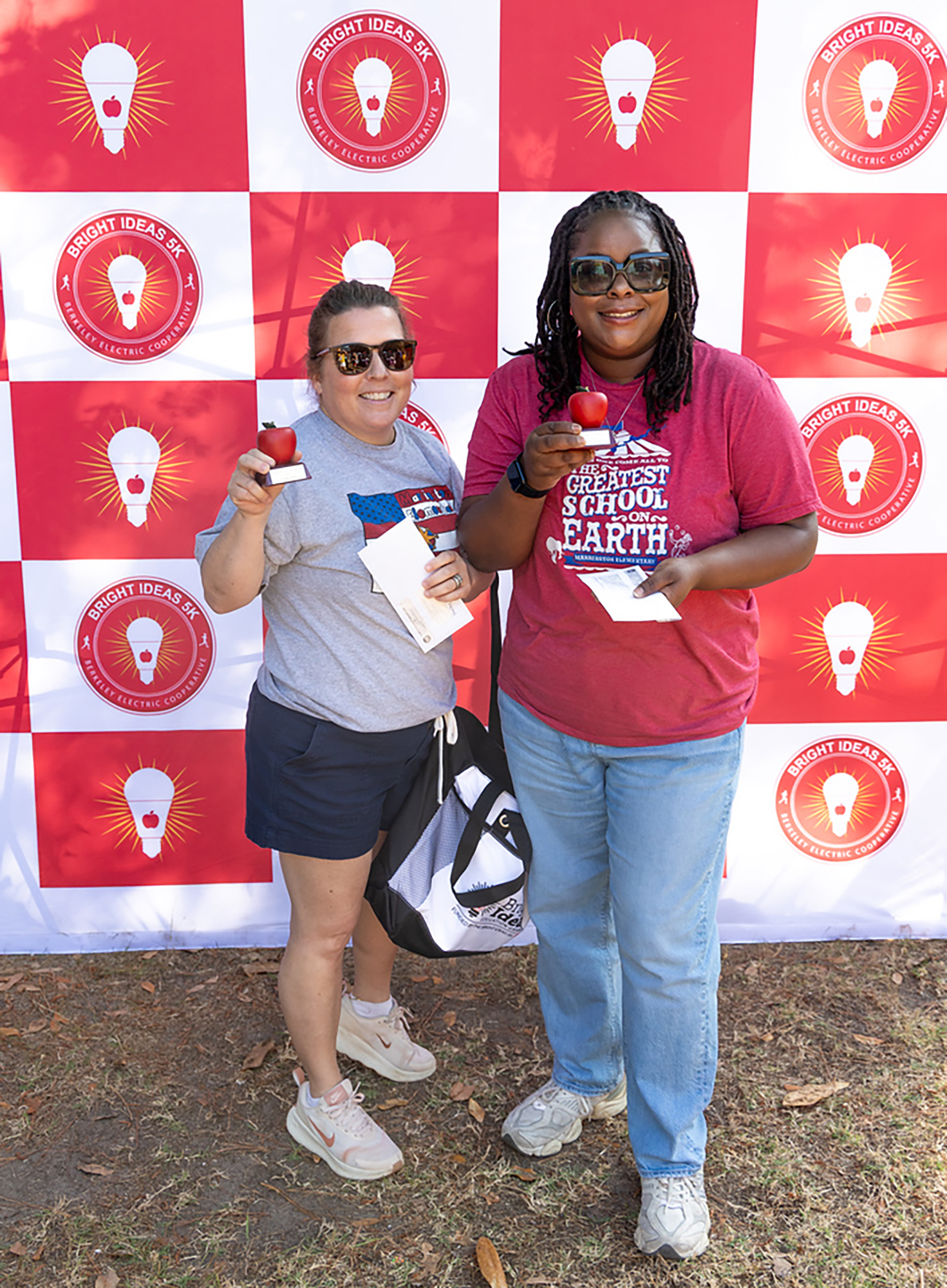Two women in front of a red and white wall with lightbulb logos. Both holding red objects.