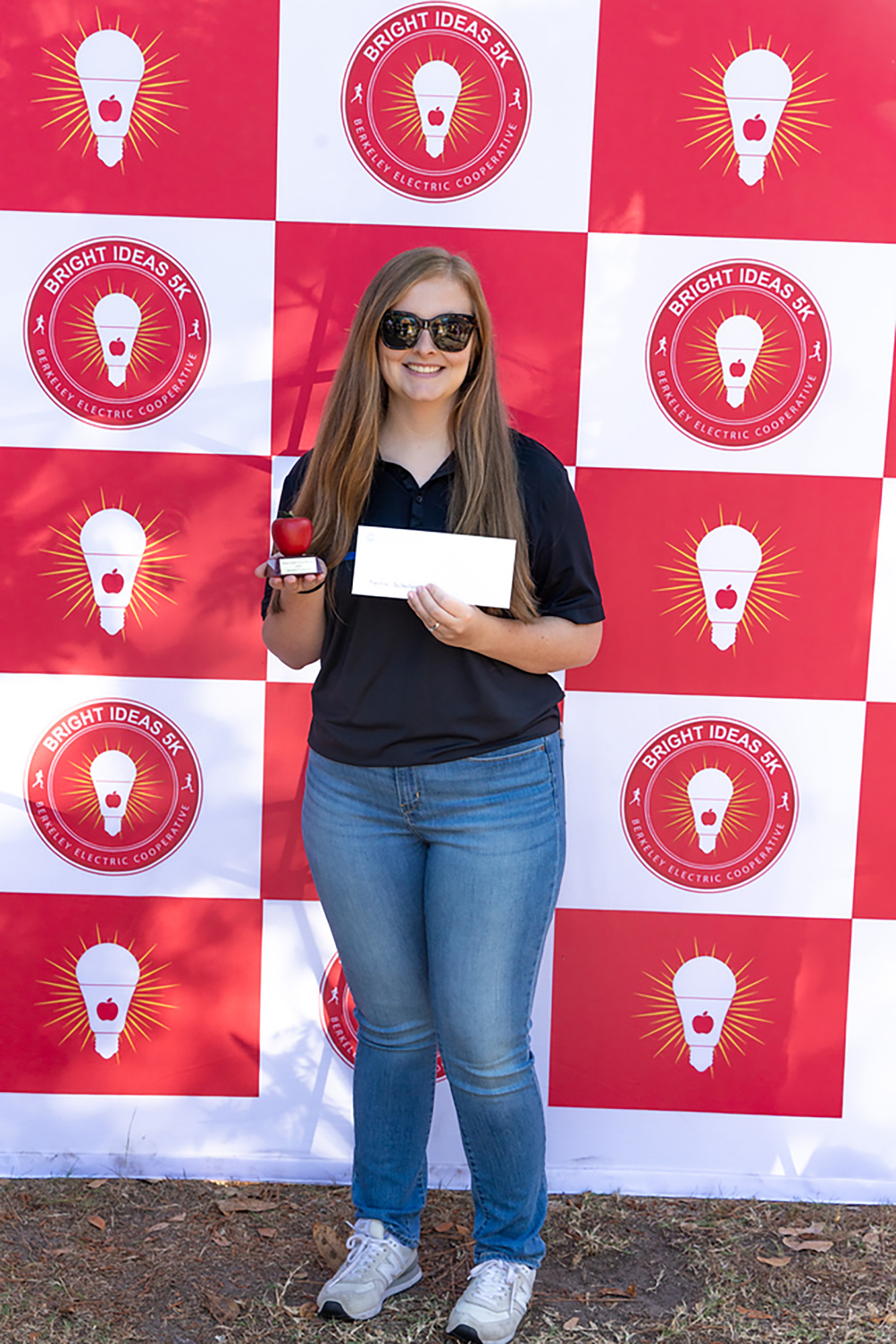 Woman in black shirt and jeans holding a certificate in front of a red, white and yellow backdrop.