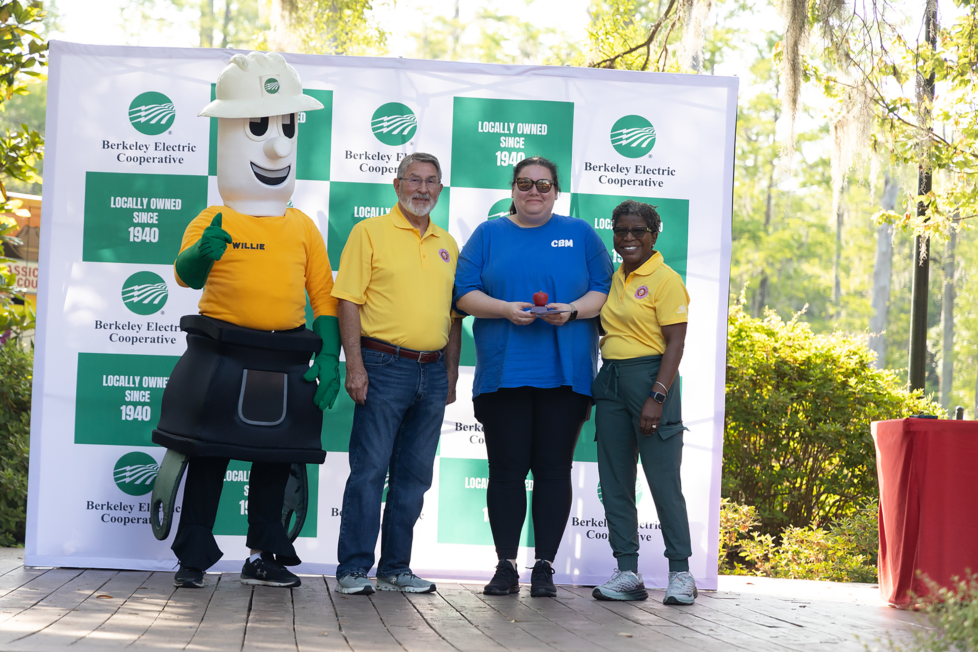 A group of four people in yellow and blue shirts stand behind a banner. Two are in costumes.