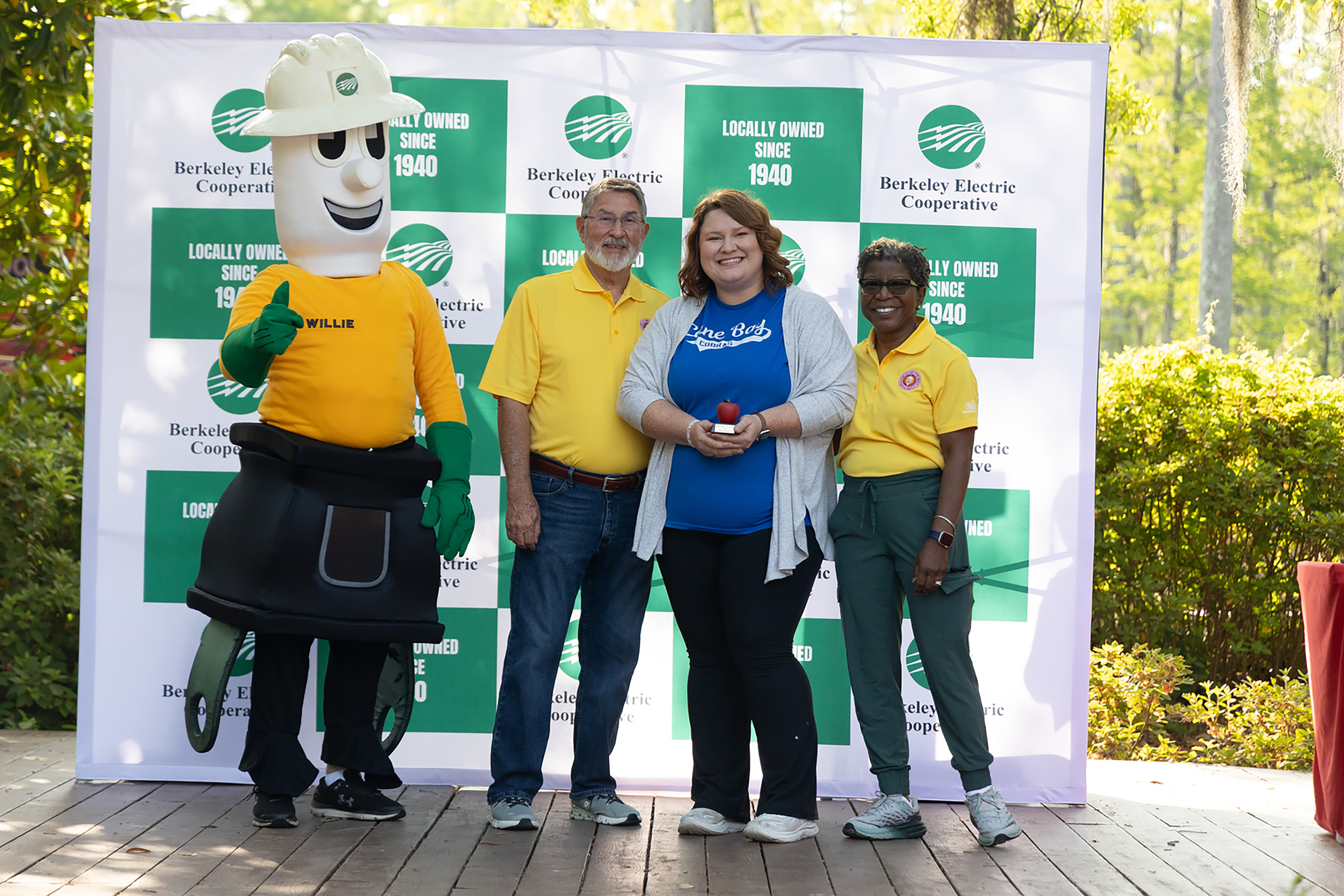 Four people in yellow shirts and pants pose in front of a green and white banner.