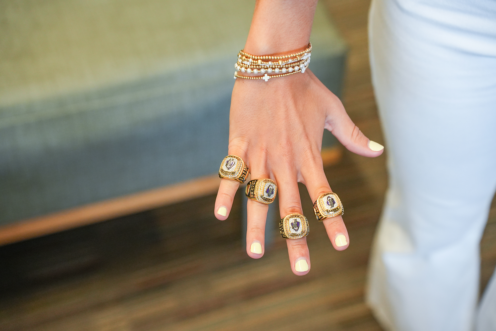 A person's hand showing three gold rings and a bracelet with a white background and wooden floor.
