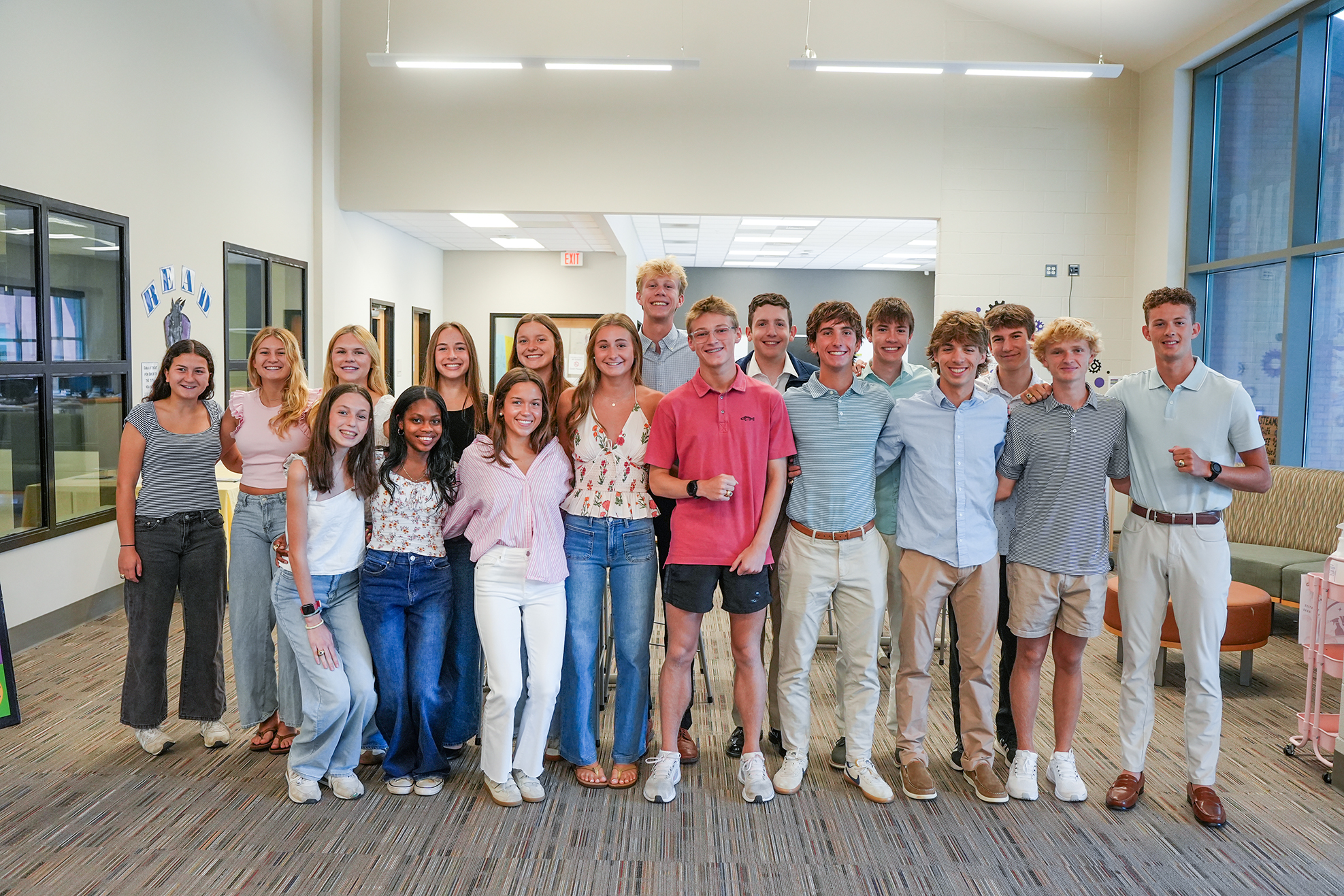 Group of young adults, both male and female, in casual summer attire posing together in a room.