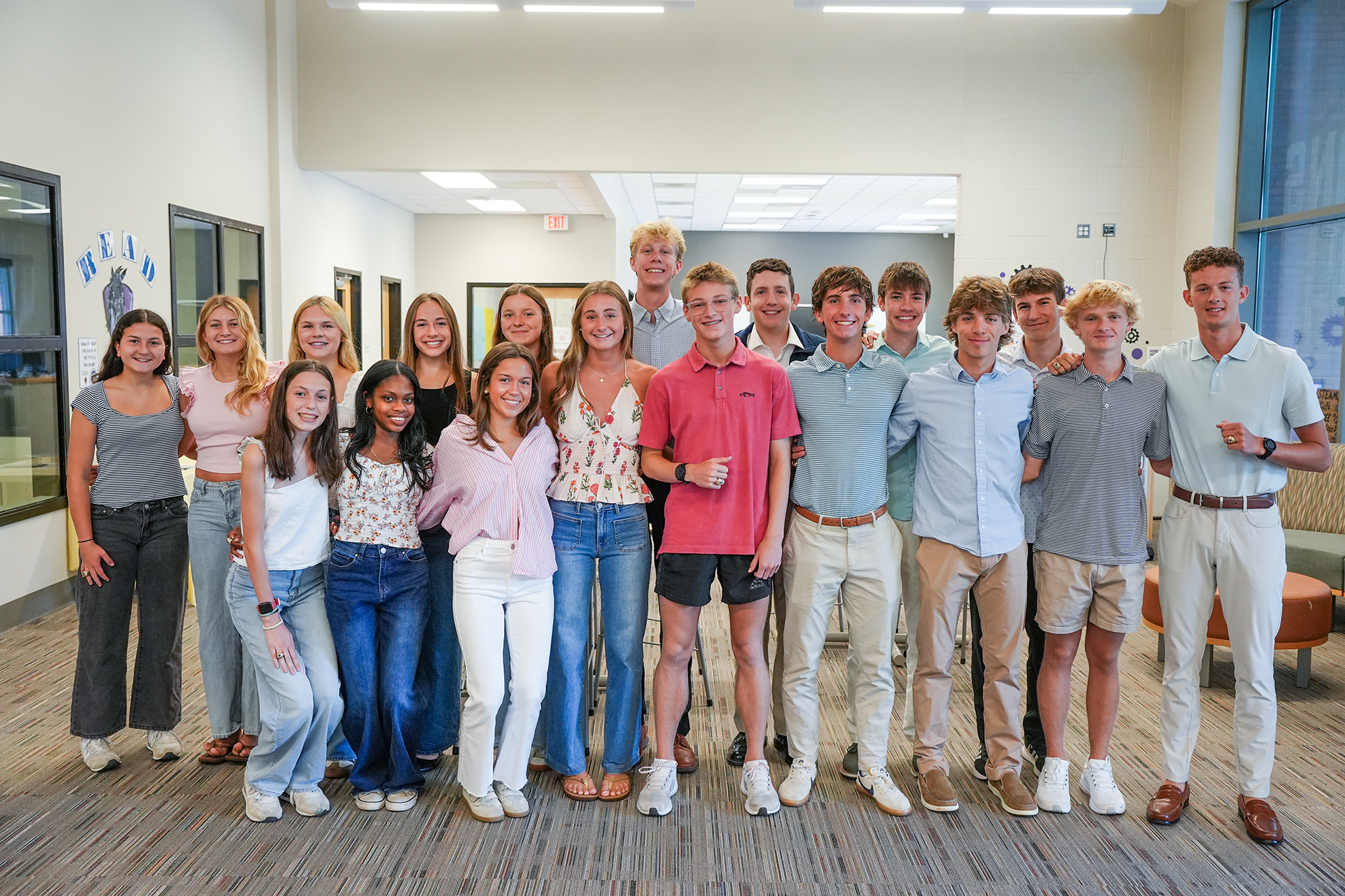 A group of young adults wearing casual clothes, including jeans and shirts, standing together in a hallway.