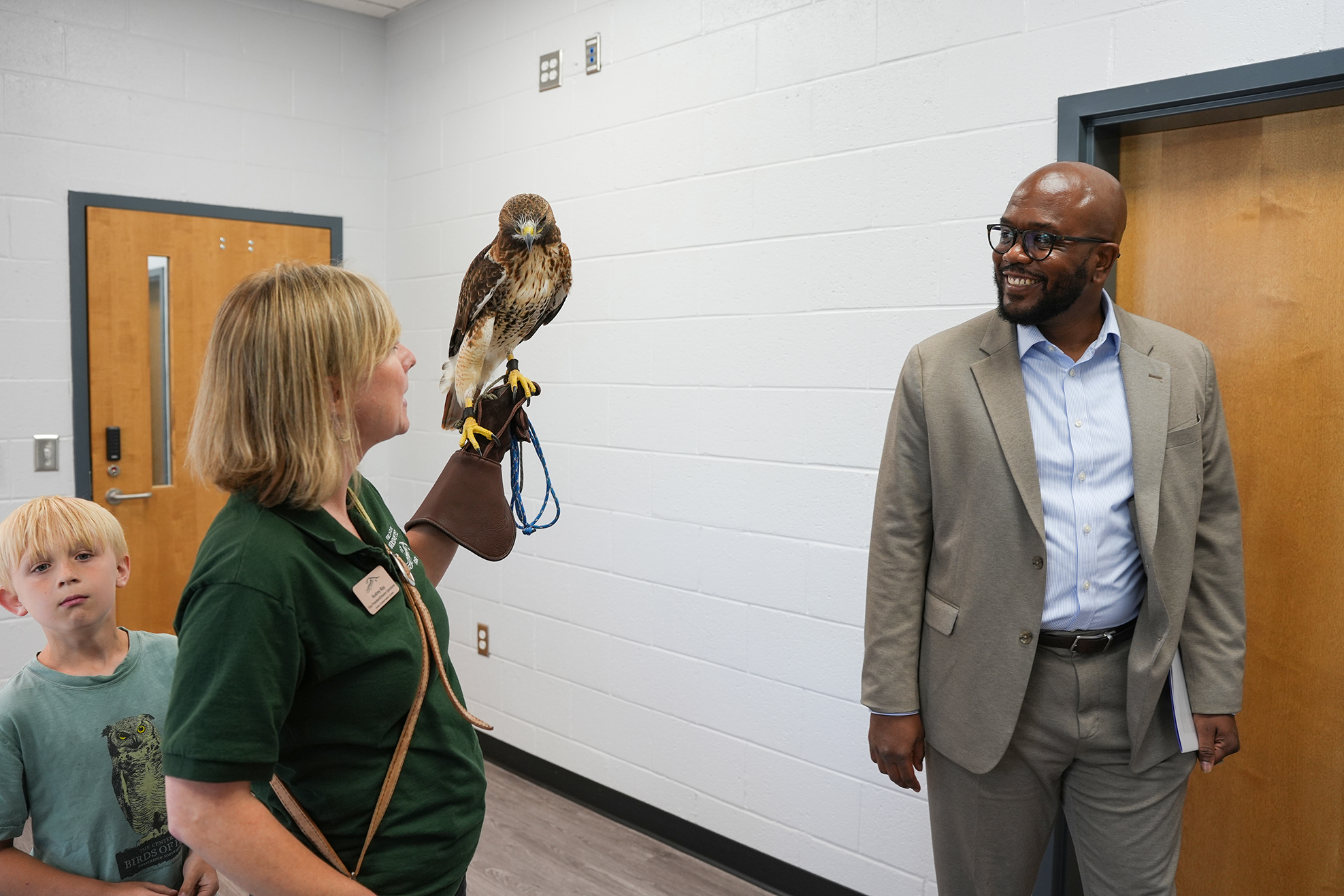 Woman holds a hawk on her arm as a man and child watch. The room has two doors.