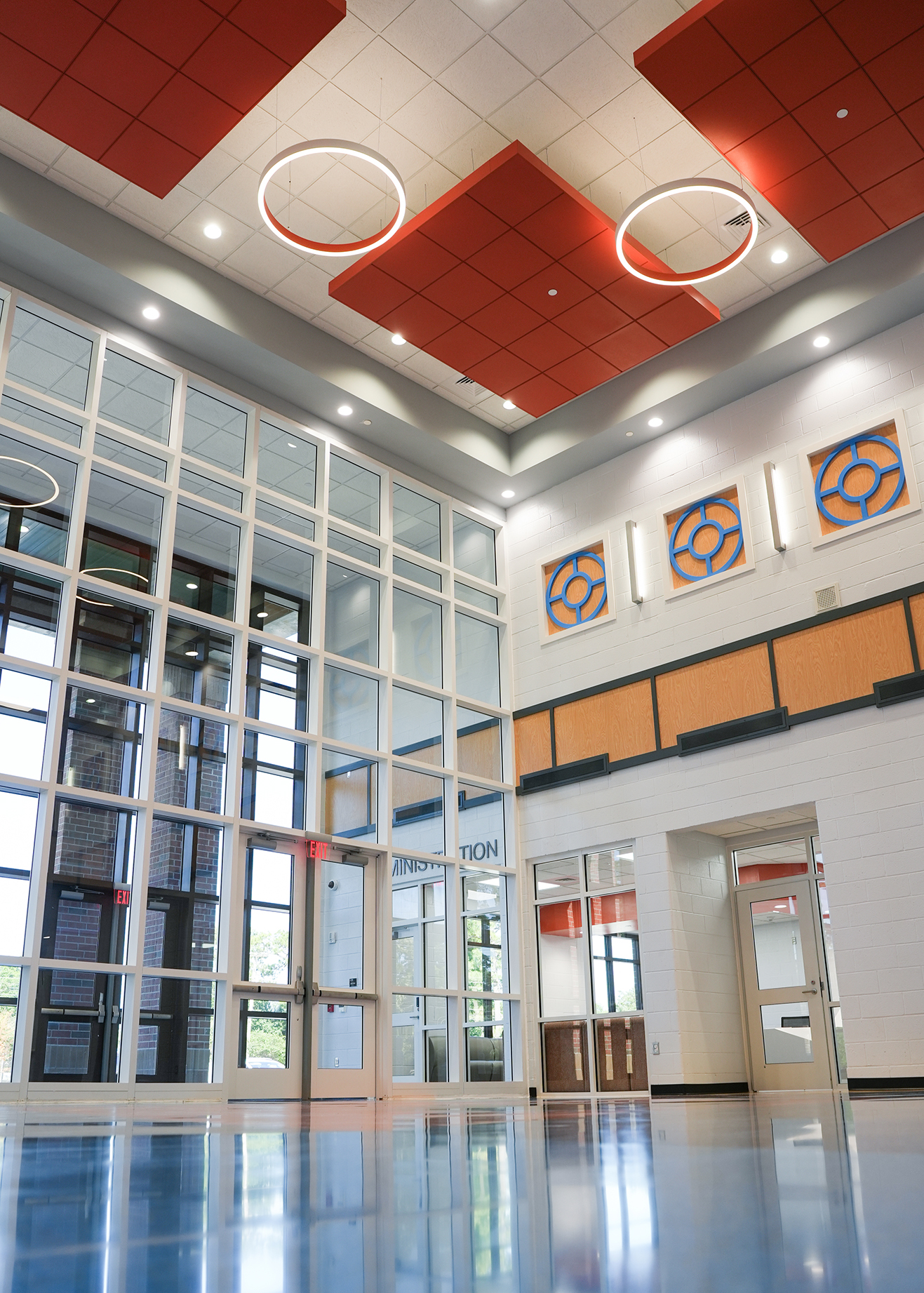 Large room with empty floors, glass walls, red ceiling panels, three circular lights, and three decorative wall panels.