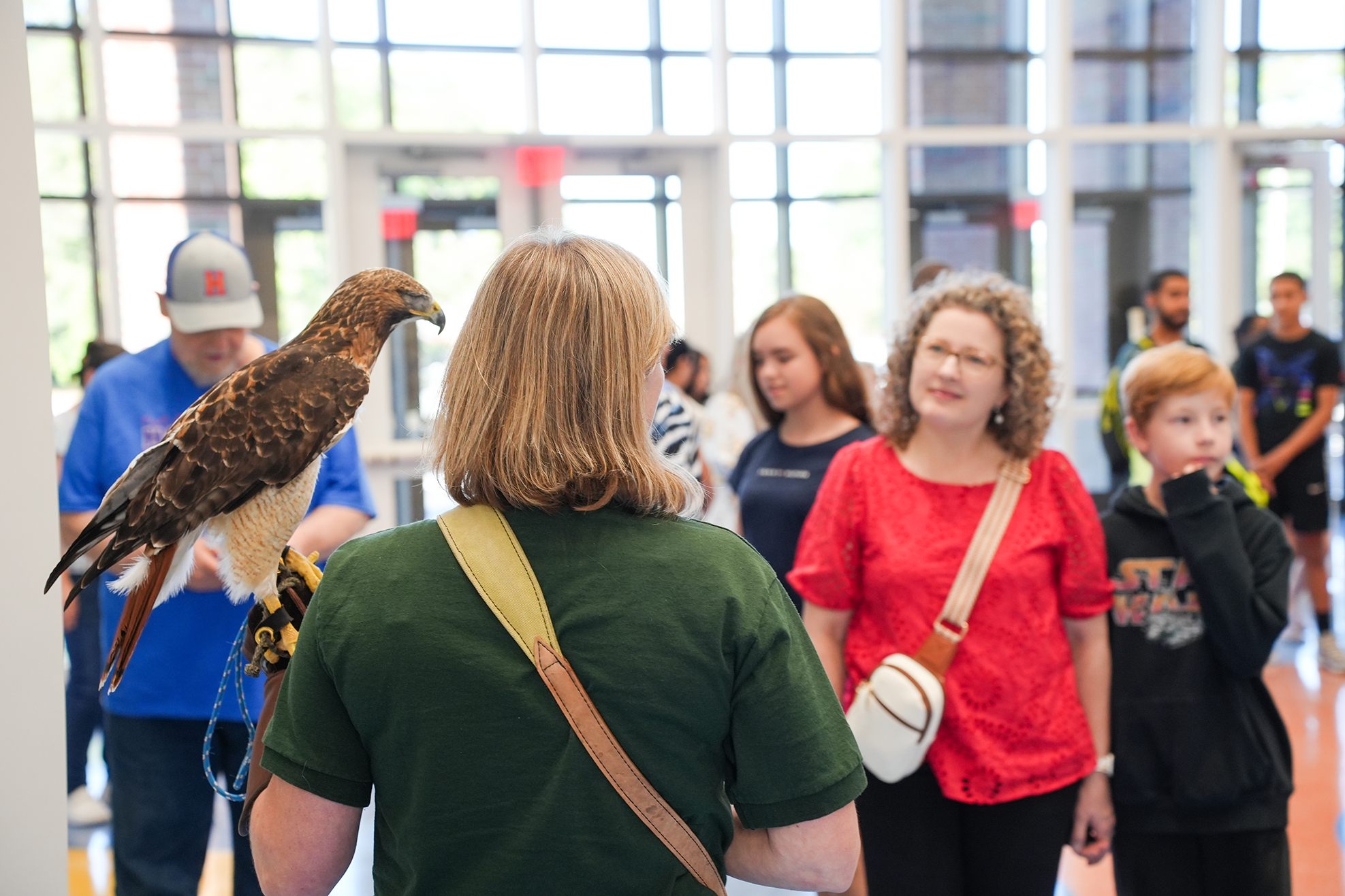 A person with a bird on their shoulder stands with others in a lobby.