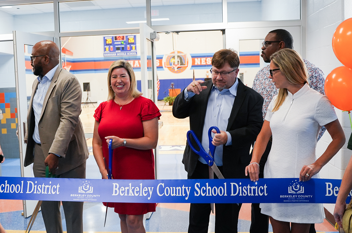 Six adults standing at a ribbon. The man and woman in the center cut it with scissors. A banner reads "Berkeley County School District".