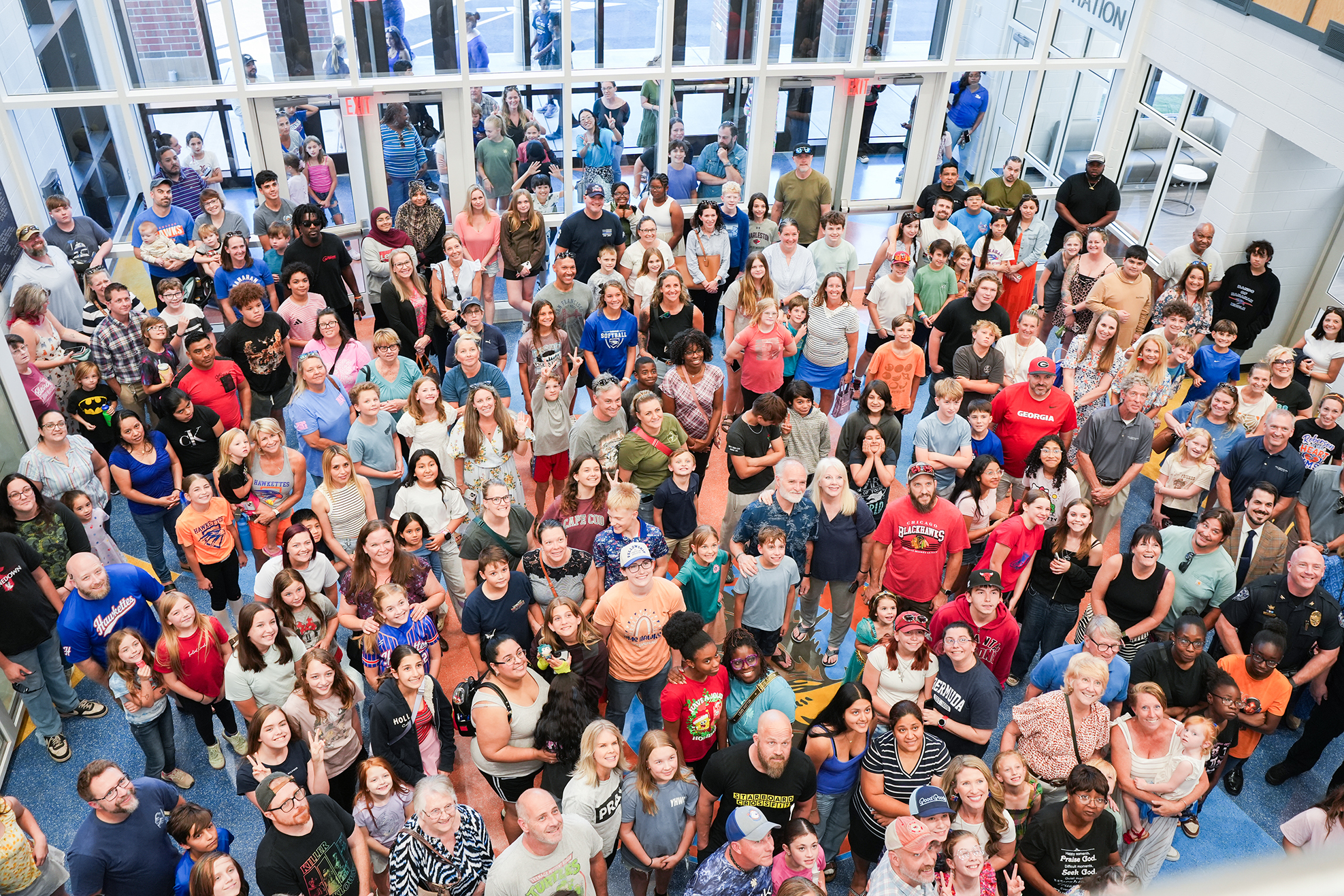 Large group of people standing in a circular formation inside a building with glass walls.