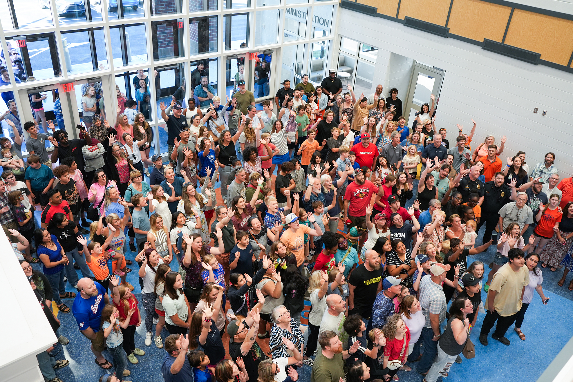 A large group of people in a modern building with glass walls, many raising their hands.