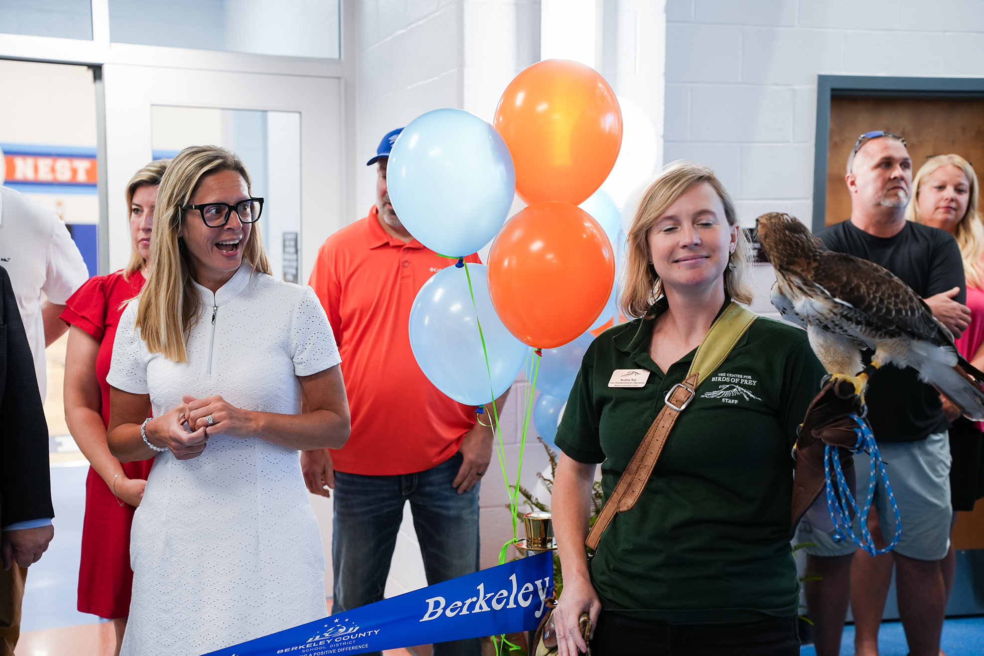 People stand around a ribbon-cutting ceremony. Two women smile; one holds a bird on her arm.