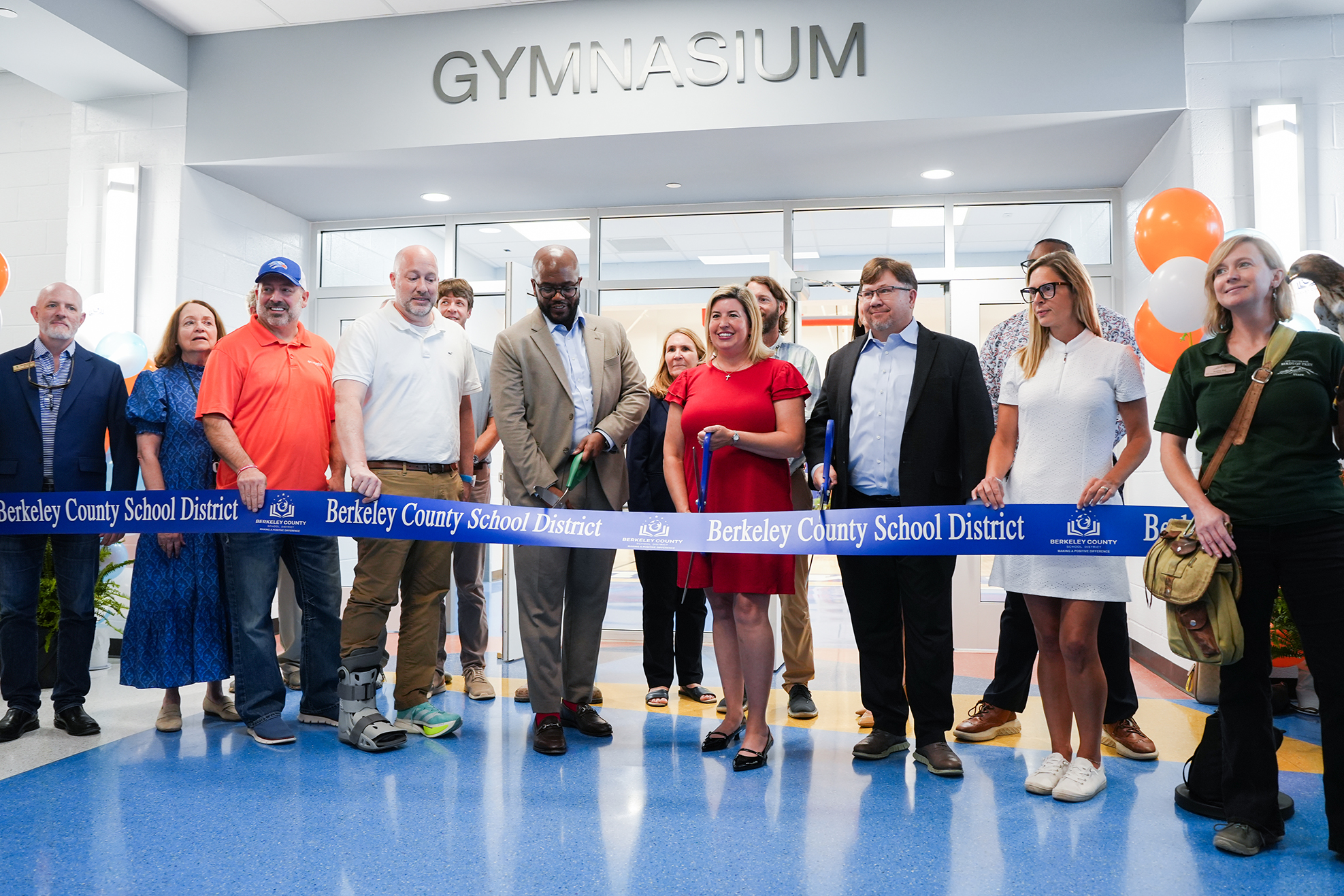 People in a gymnasium with a blue ribbon, standing behind it. A sign above says "GYMNASIUM."