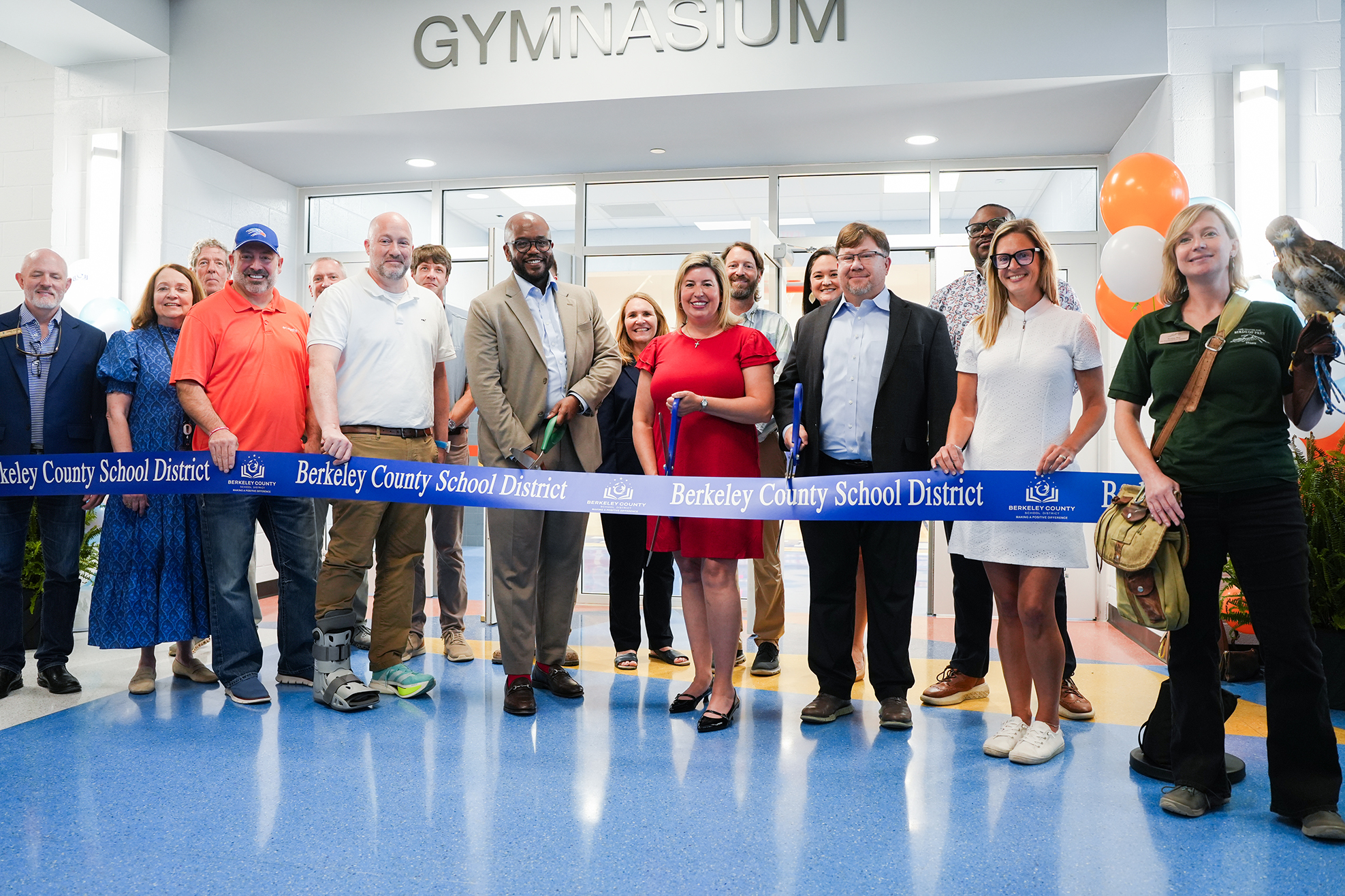 A group of people stand around a blue ribbon labeled "Gymnasium" with a large bird nearby.