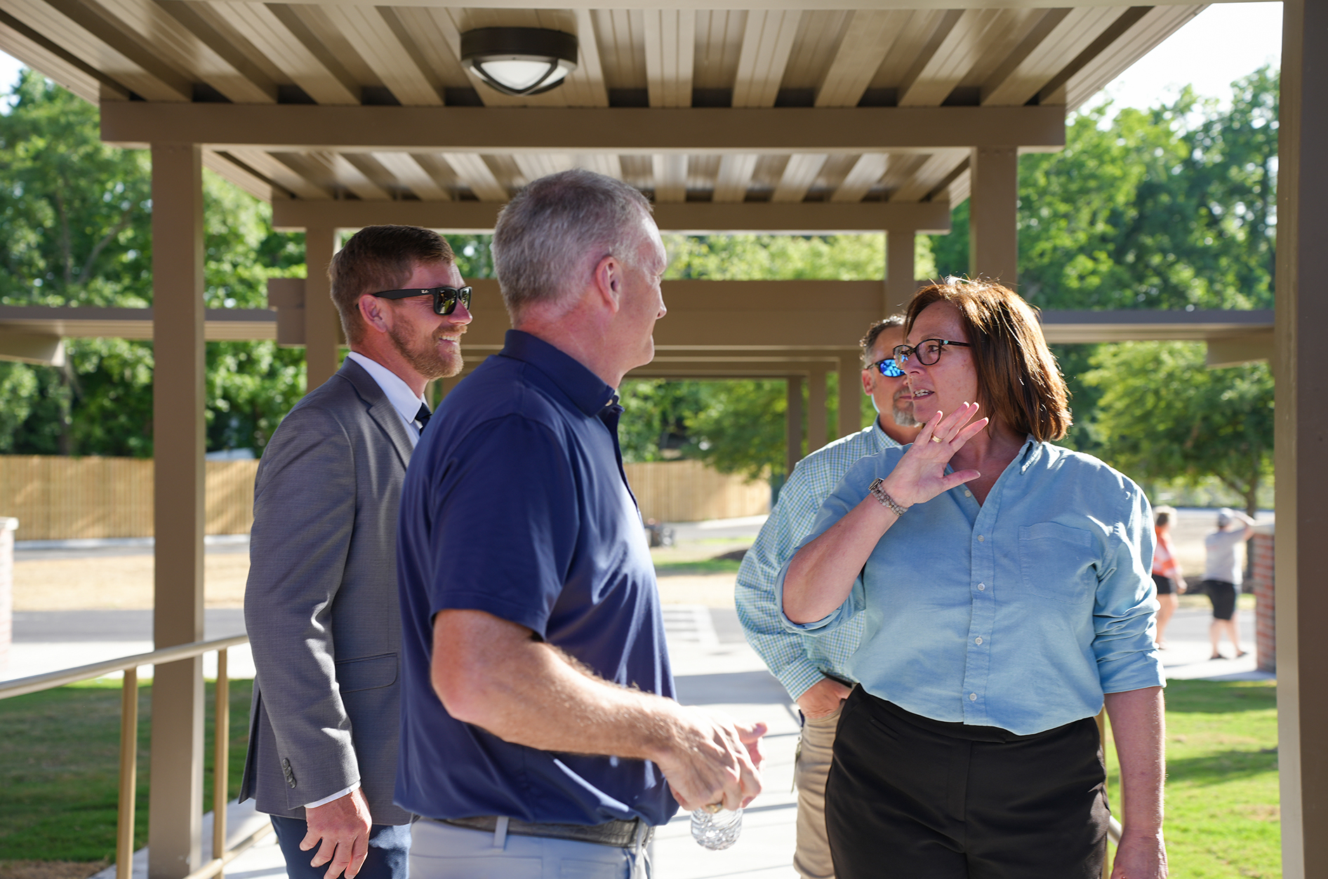 Four people under a metal structure with a roof. Two men and two women, one wearing glasses.