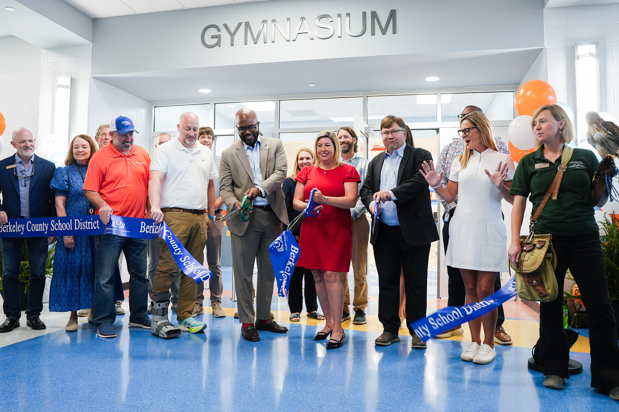 A group of adults, some wearing hats, stands around a ribbon at a ribbon-cutting event.