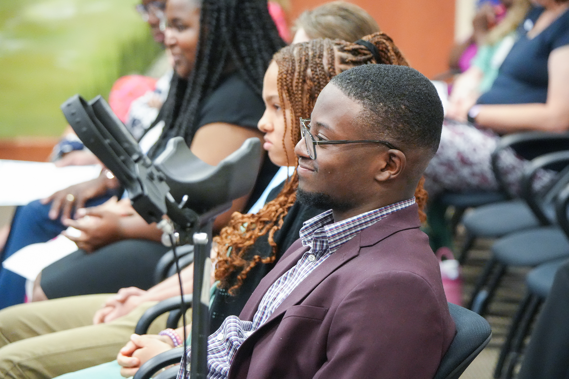 A group of people at a gathering. One man in a suit is seated with a microphone on a stand.