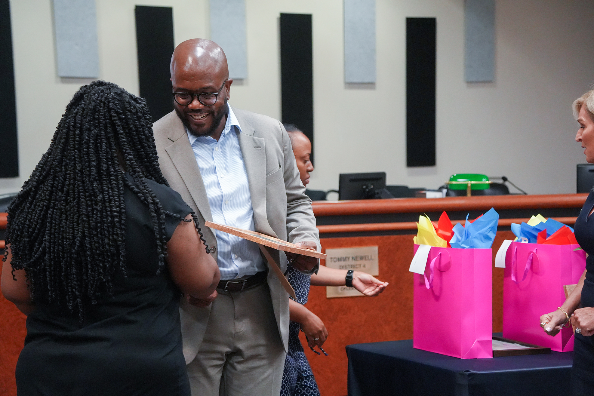 A group of people gathered around a table with bags; a person holds a certificate while another woman smiles.