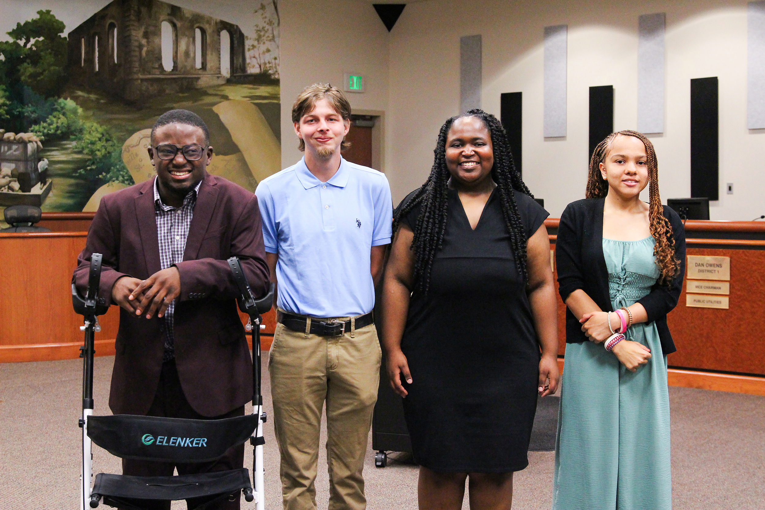 Four people in formal attire pose for a photo in a room. One uses a wheelchair.