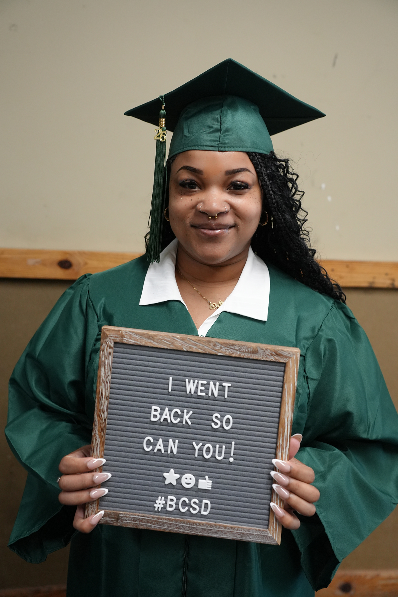Woman in a green gown holds a sign that reads, "I WENT BACK SO YOU CAN TOO! #BCSd".