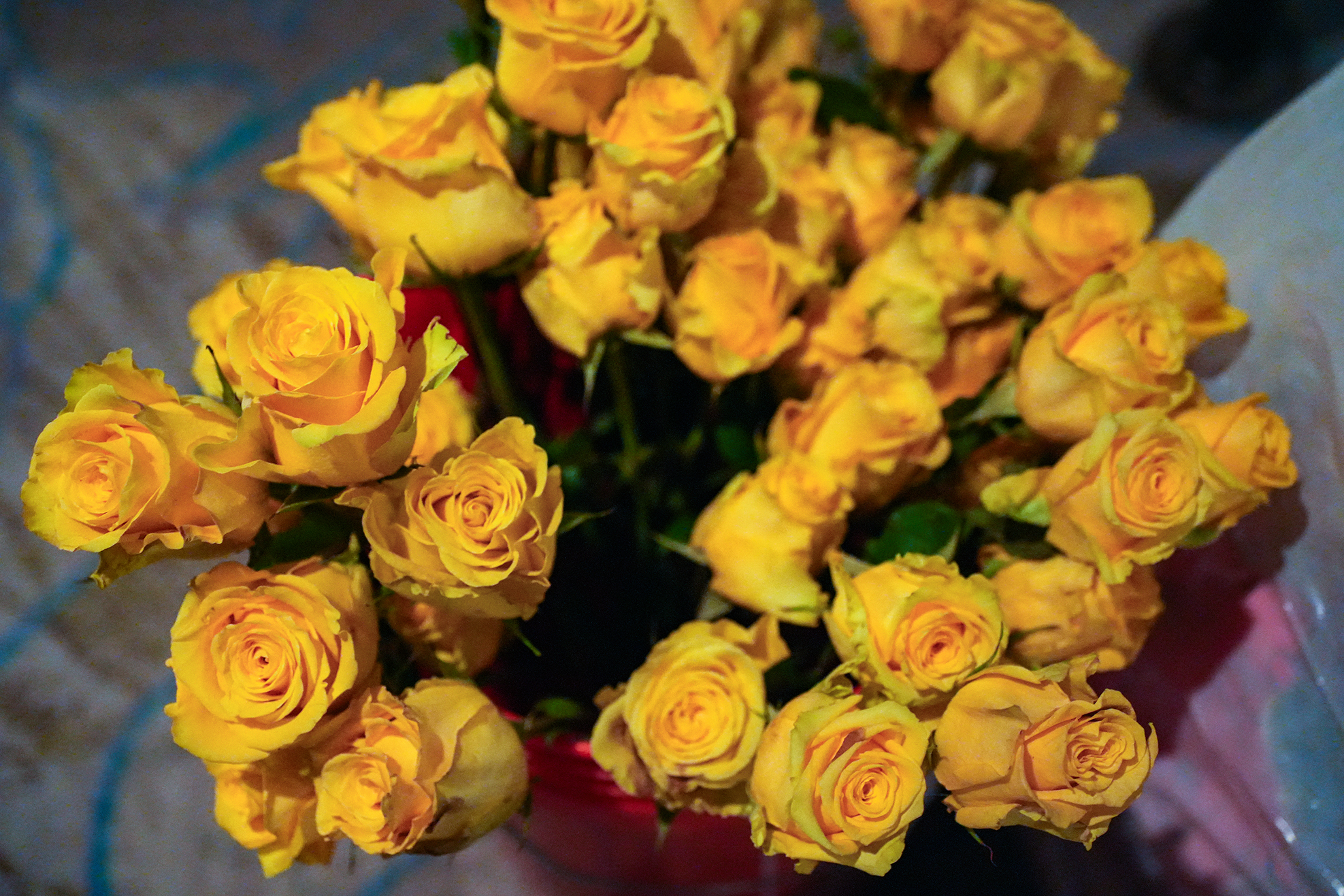 A large arrangement of yellow roses in a red vase, displayed on a patterned surface.