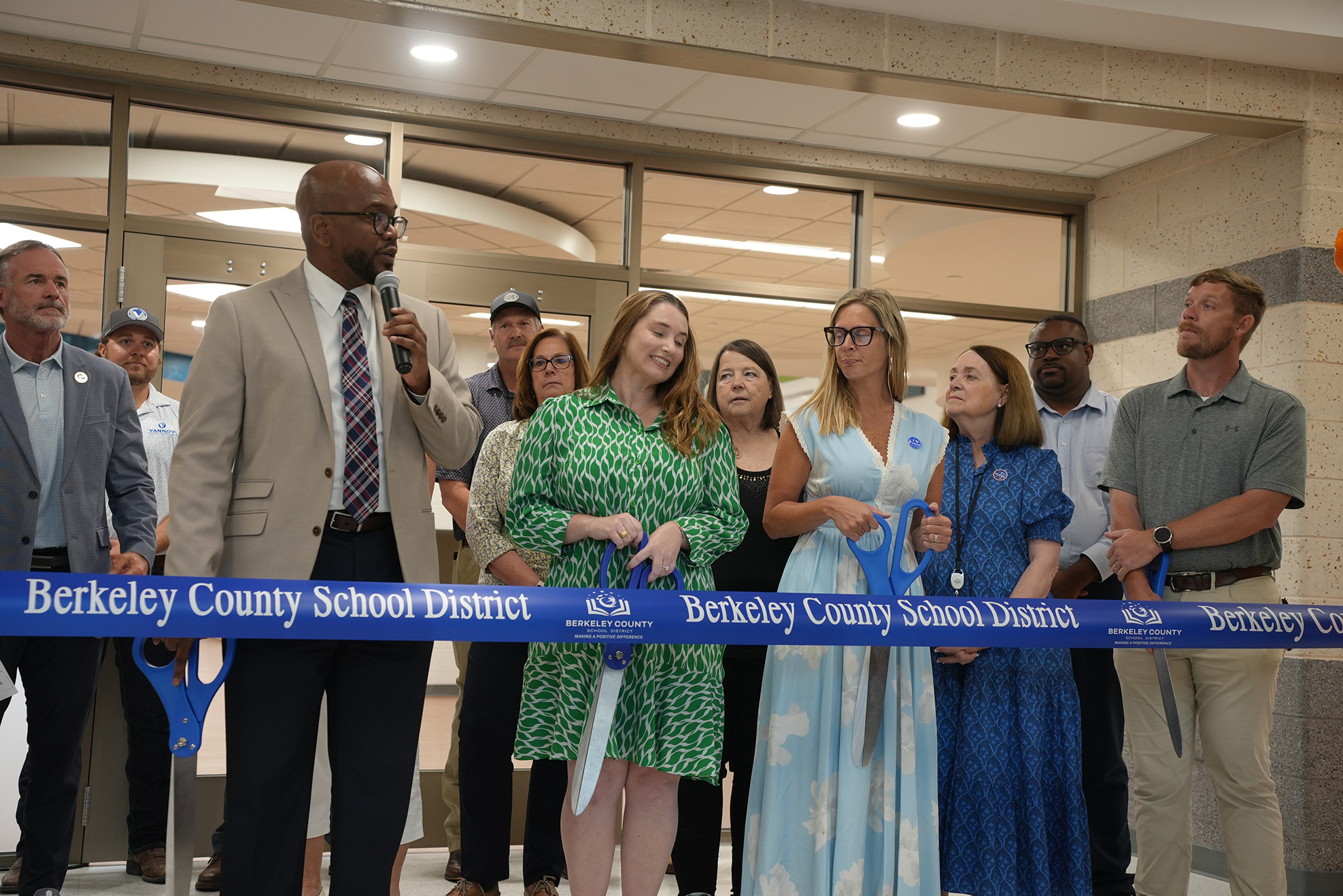 A group stands before a blue ribbon with the words "Berkeley County School District." They hold scissors, ready to cut the ribbon.