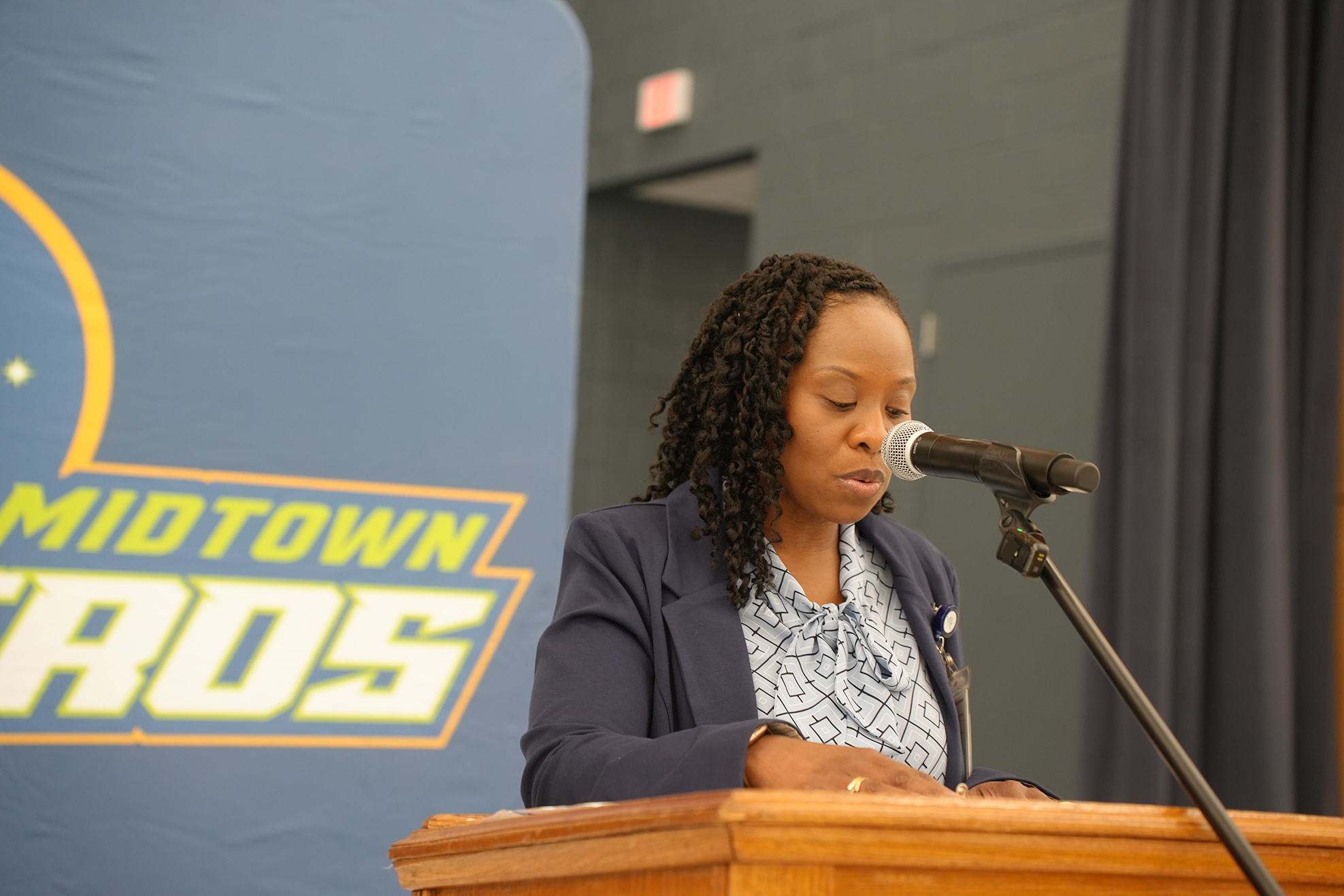 Person speaking at a podium, a microphone in front, a Midtown Cross banner behind them.