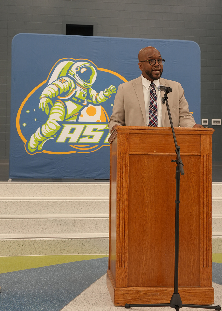 Man stands at a podium with a microphone in front of a banner featuring an astronaut.