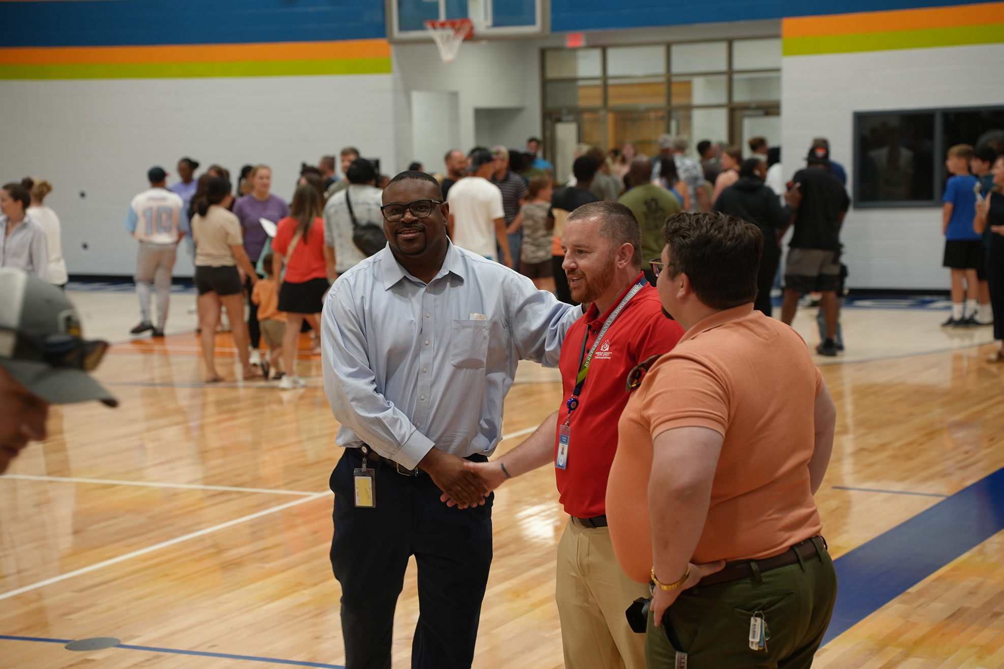 Indoor basketball court with a man in a blue shirt and black pants shaking hands with a man in a red shirt.