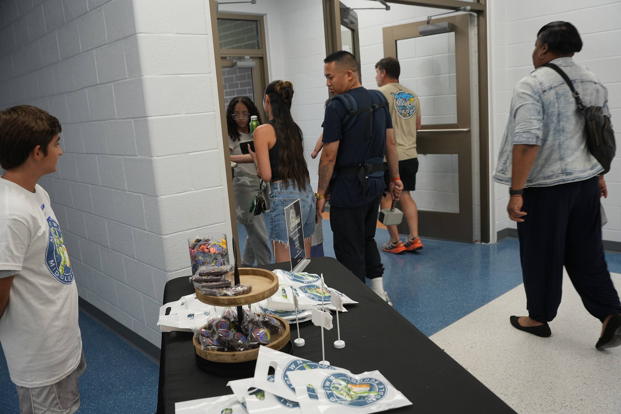 A hallway with people at a table displaying various items. A table holds cups, bags, and other objects.