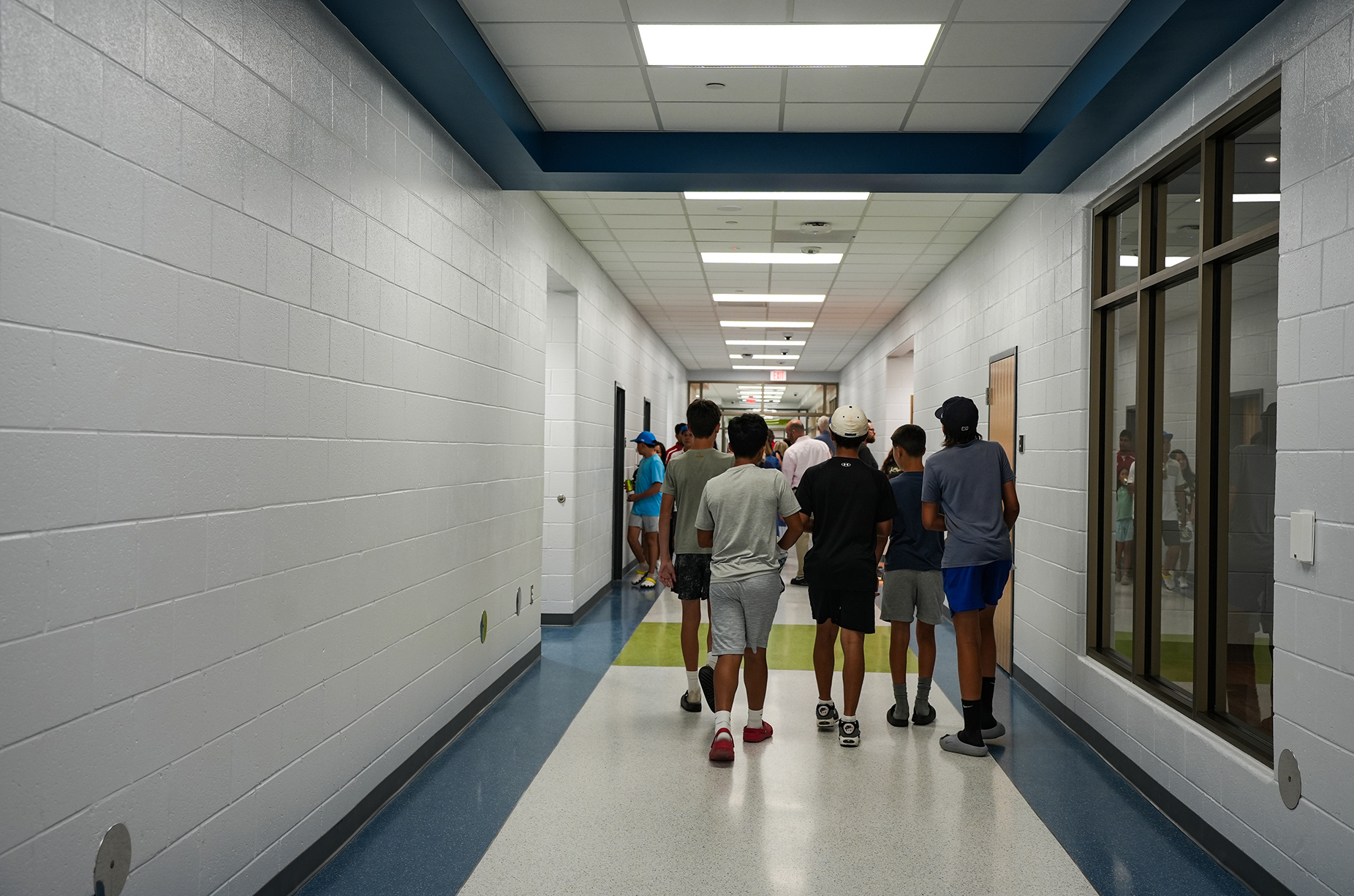 A group of people walk through a hallway with white walls, blue trim, and a blue floor.