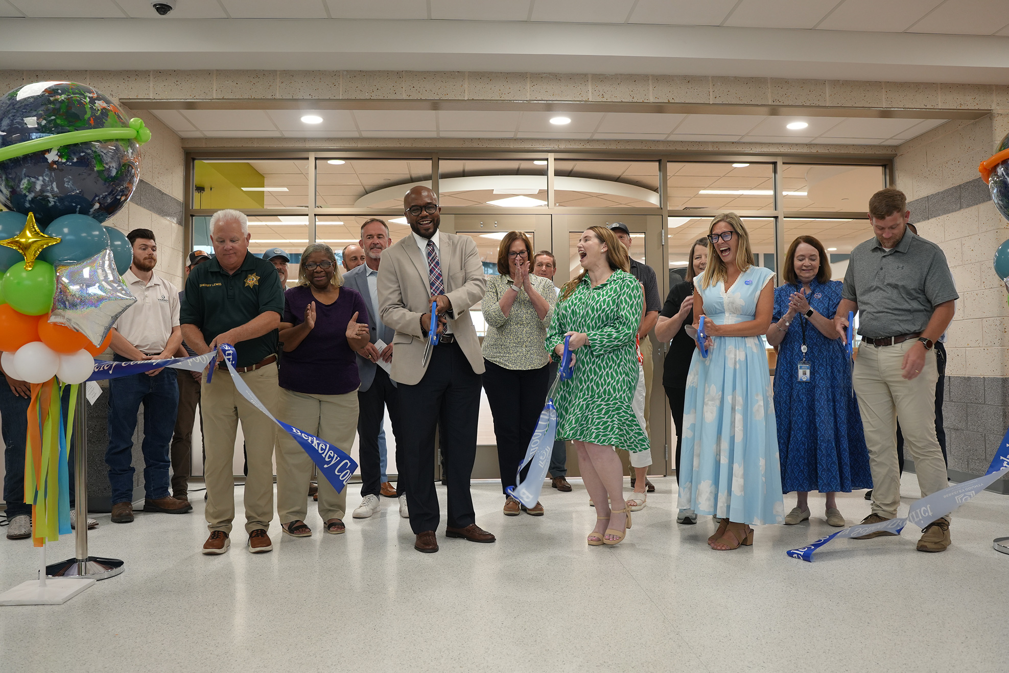 A group of people stand behind a ribbon, holding it, with two individuals in front cutting it.