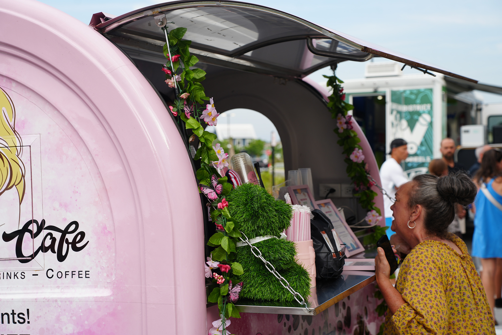 A pink food truck decorated with flowers, with a woman in yellow standing at the counter.