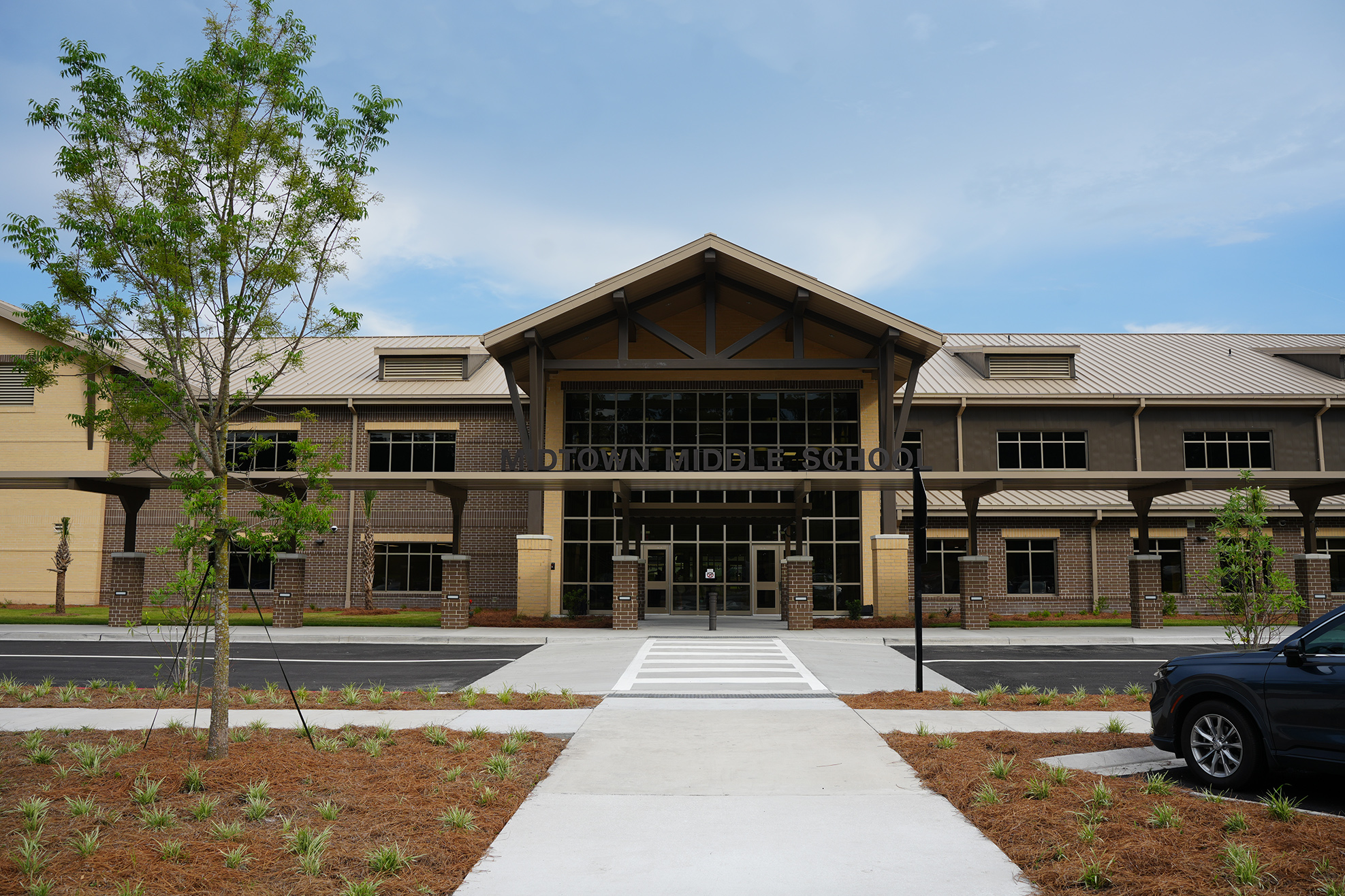 Building with large windows and entrance with a tree and car parked on the side.