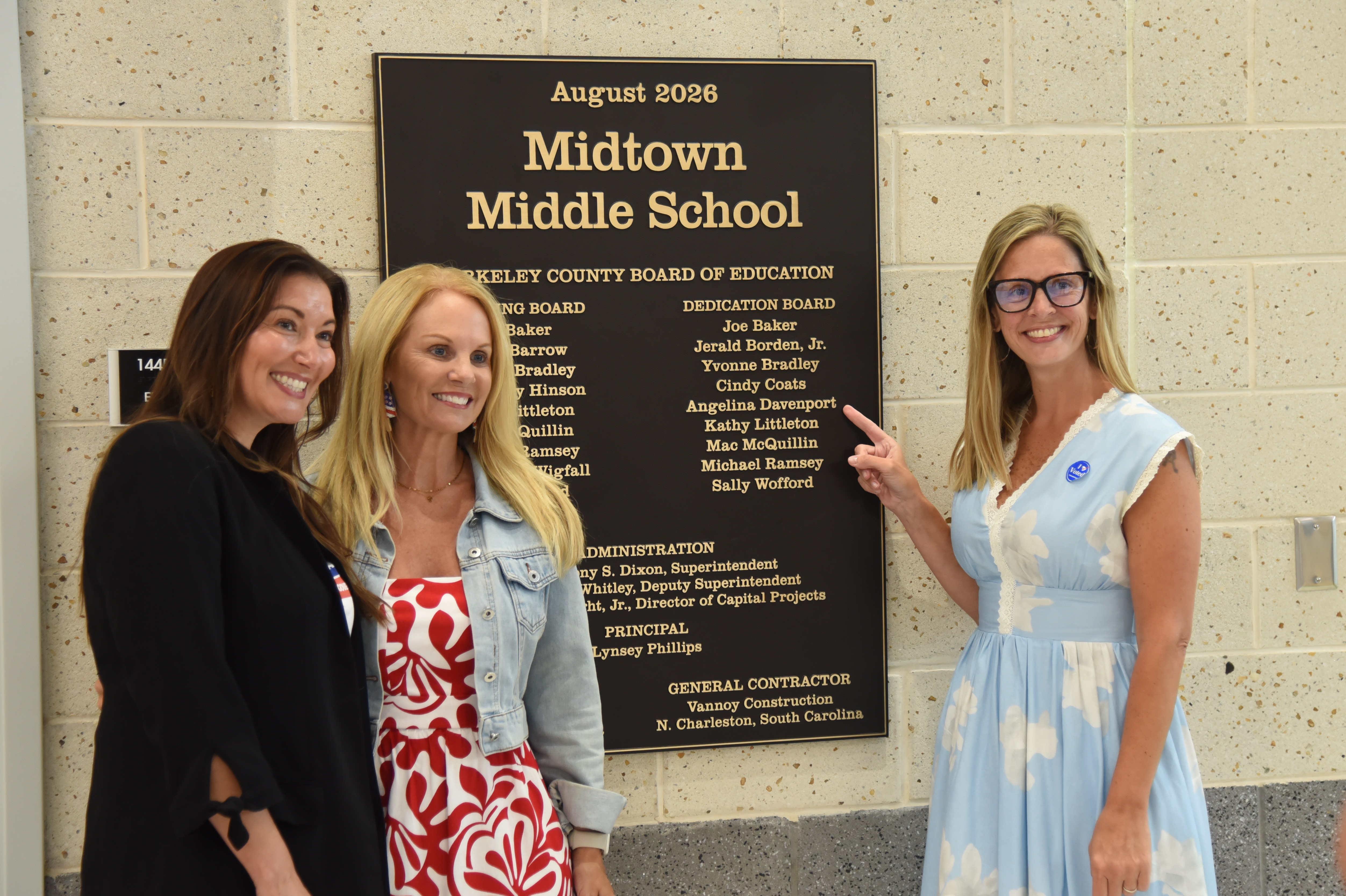 Three women stand next to a sign that reads "August 2008 Midtown Middle School" on a stone wall.