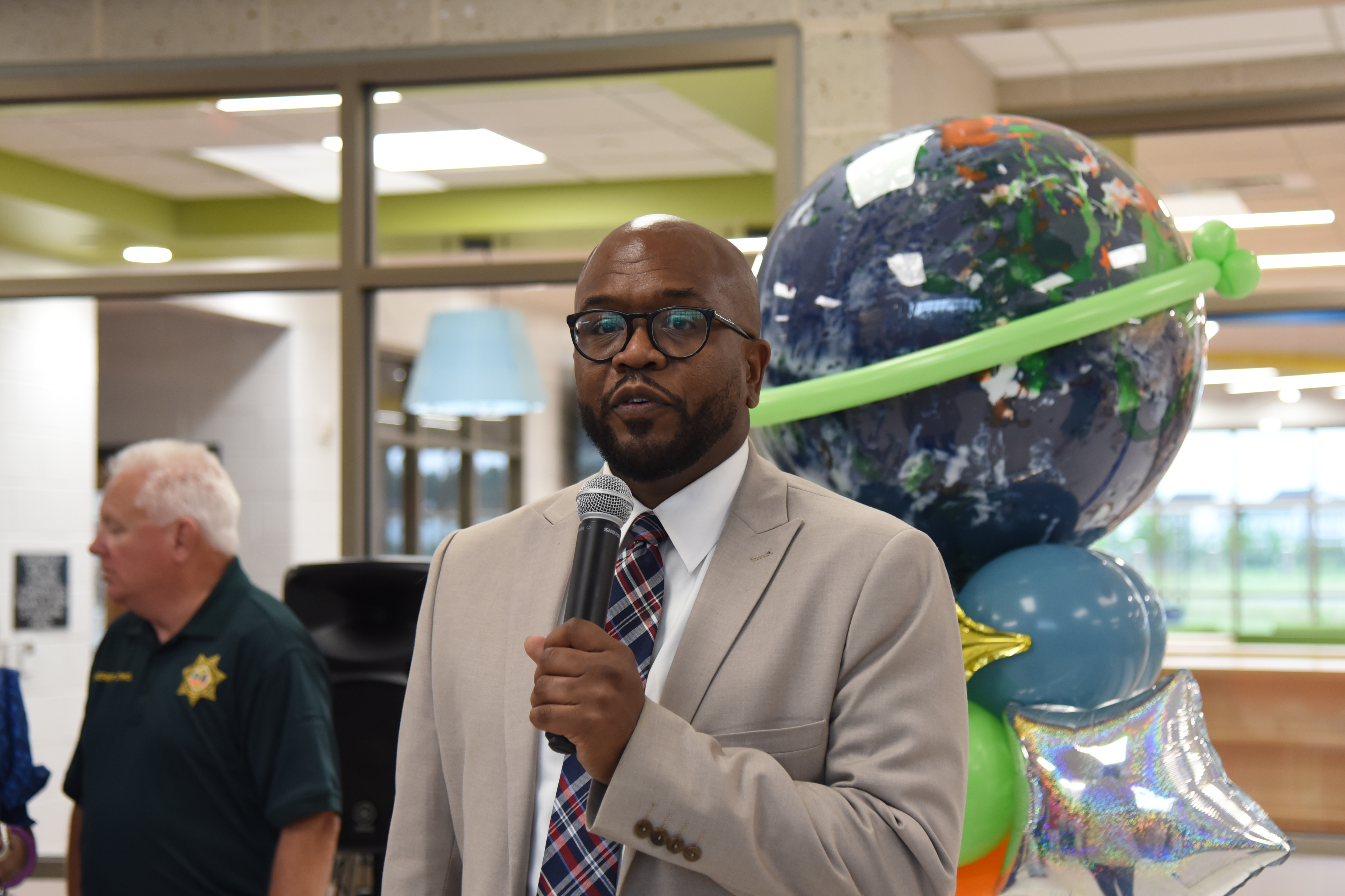 A man speaks into a microphone in an office, with a large Earth balloon behind him.