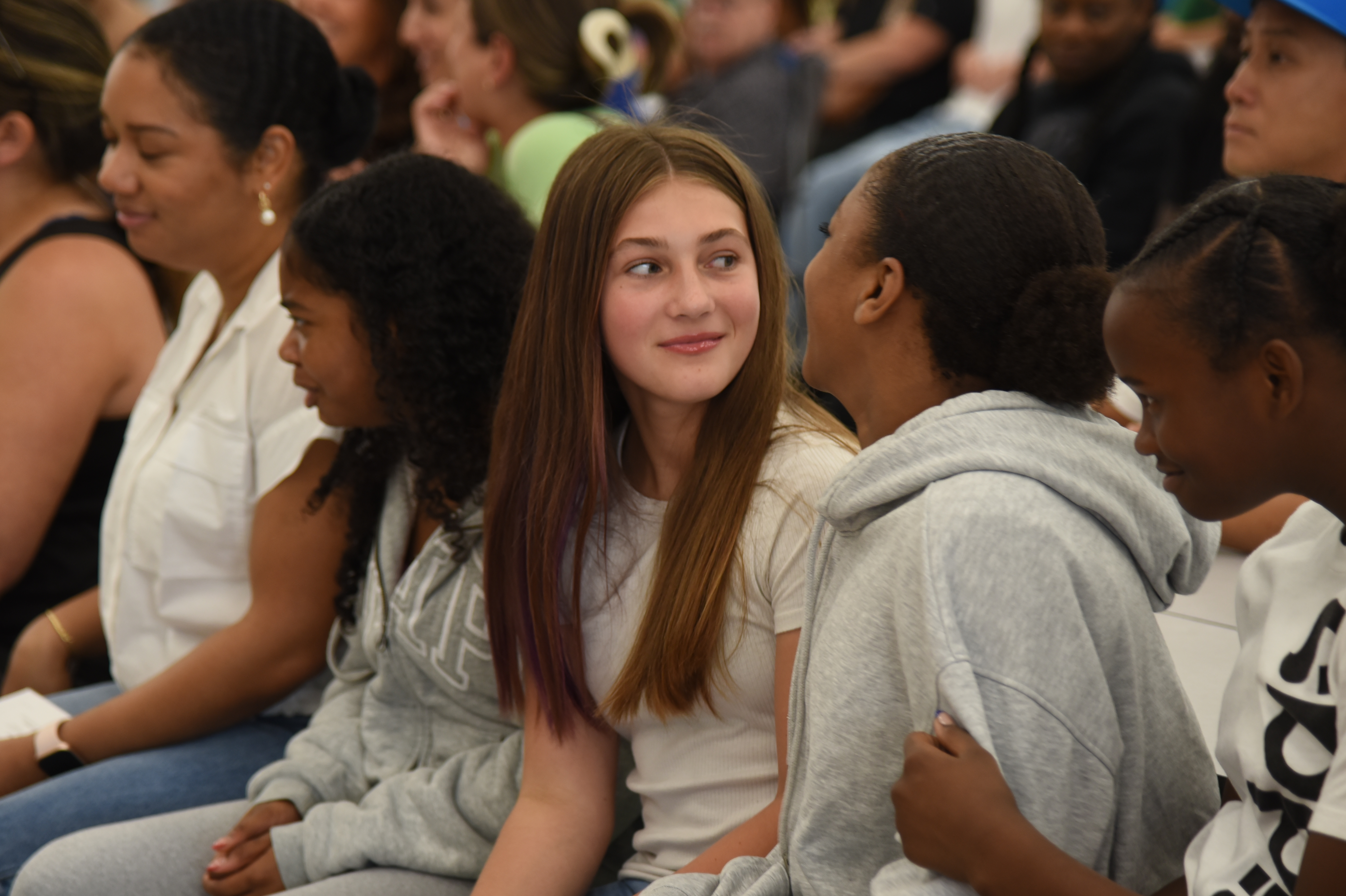 Group of people sit in rows, including one woman with long dark hair and a white shirt.