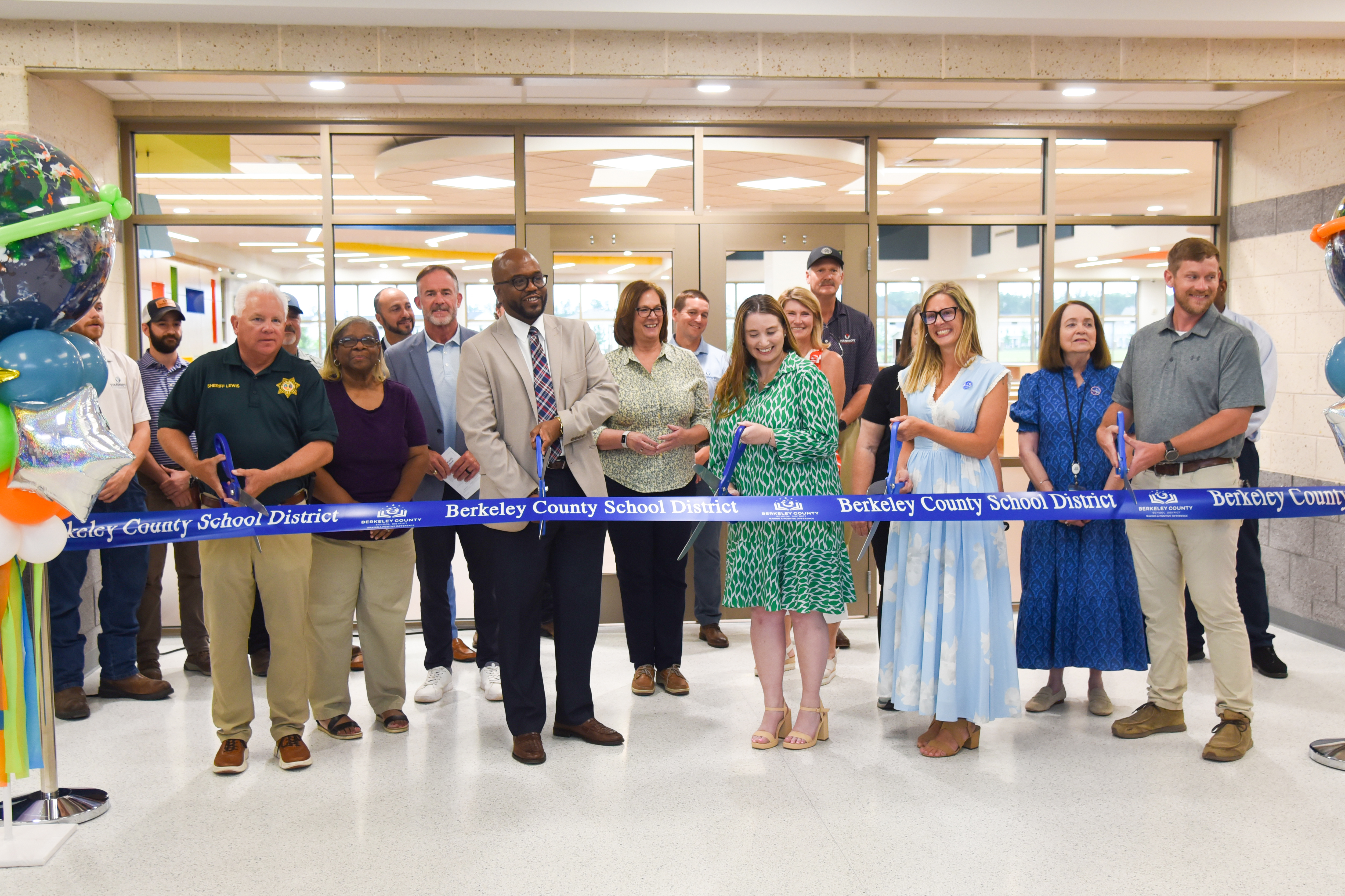 A group of people gathered for a ribbon-cutting ceremony. They hold a long blue ribbon.
