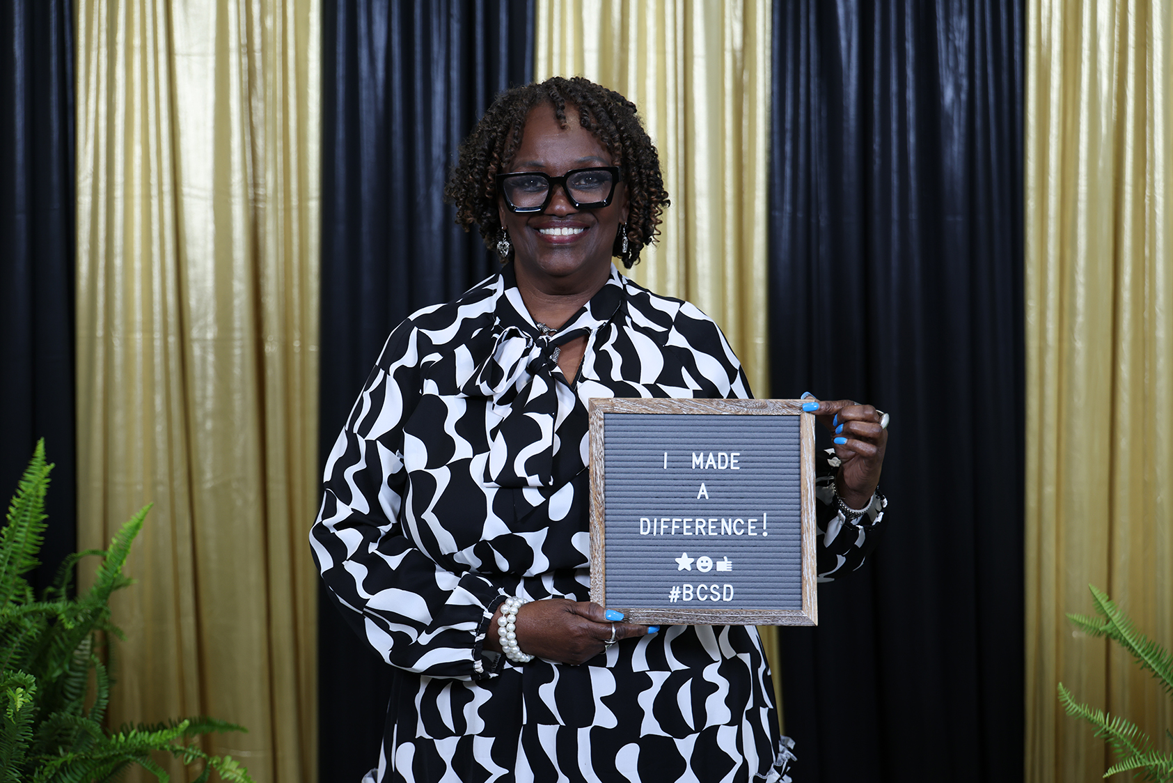 Woman in black and white outfit holds a sign with "I Made a Difference" in front of black and gold backdrop.