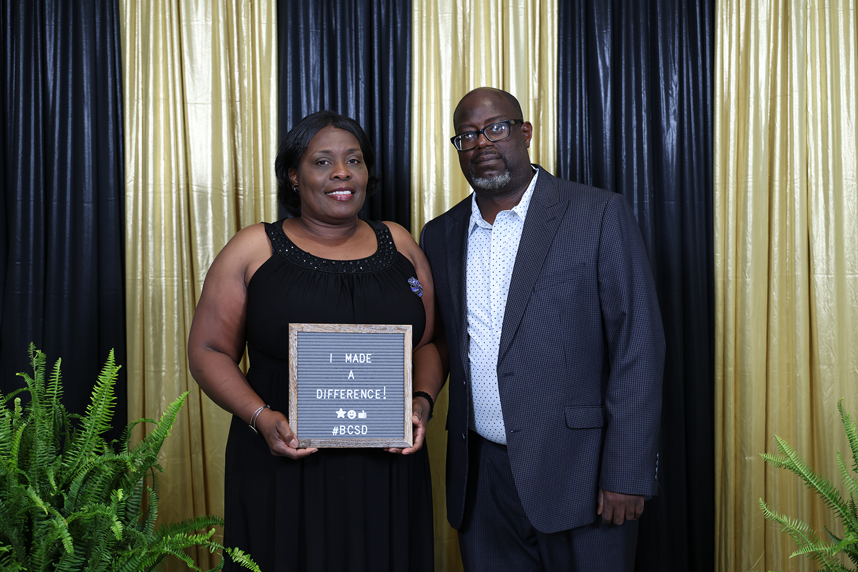 A woman in a black dress and a man in a gray suit stand with a plaque.