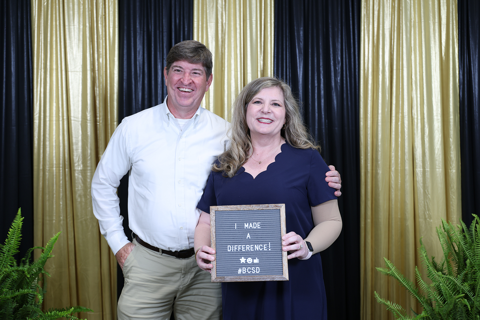 A man and woman smile for a photo while a woman holds a plaque with the message "I MADE A DIFFERENCE."