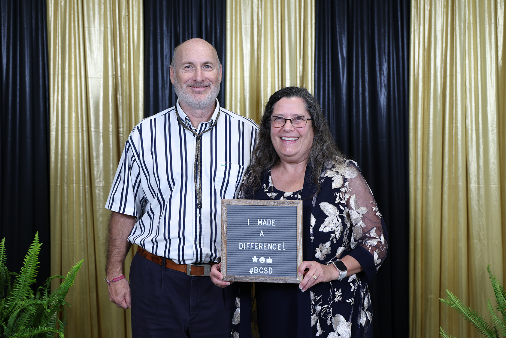 A man and woman standing together holding a framed plaque with the text "I Made a Difference".