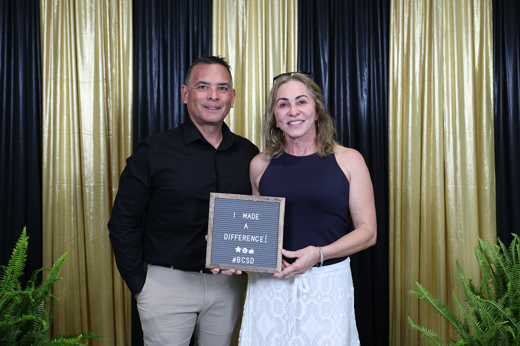 Man and woman holding a plaque that reads, "I made a difference." They are smiling in front of a black and gold backdrop.