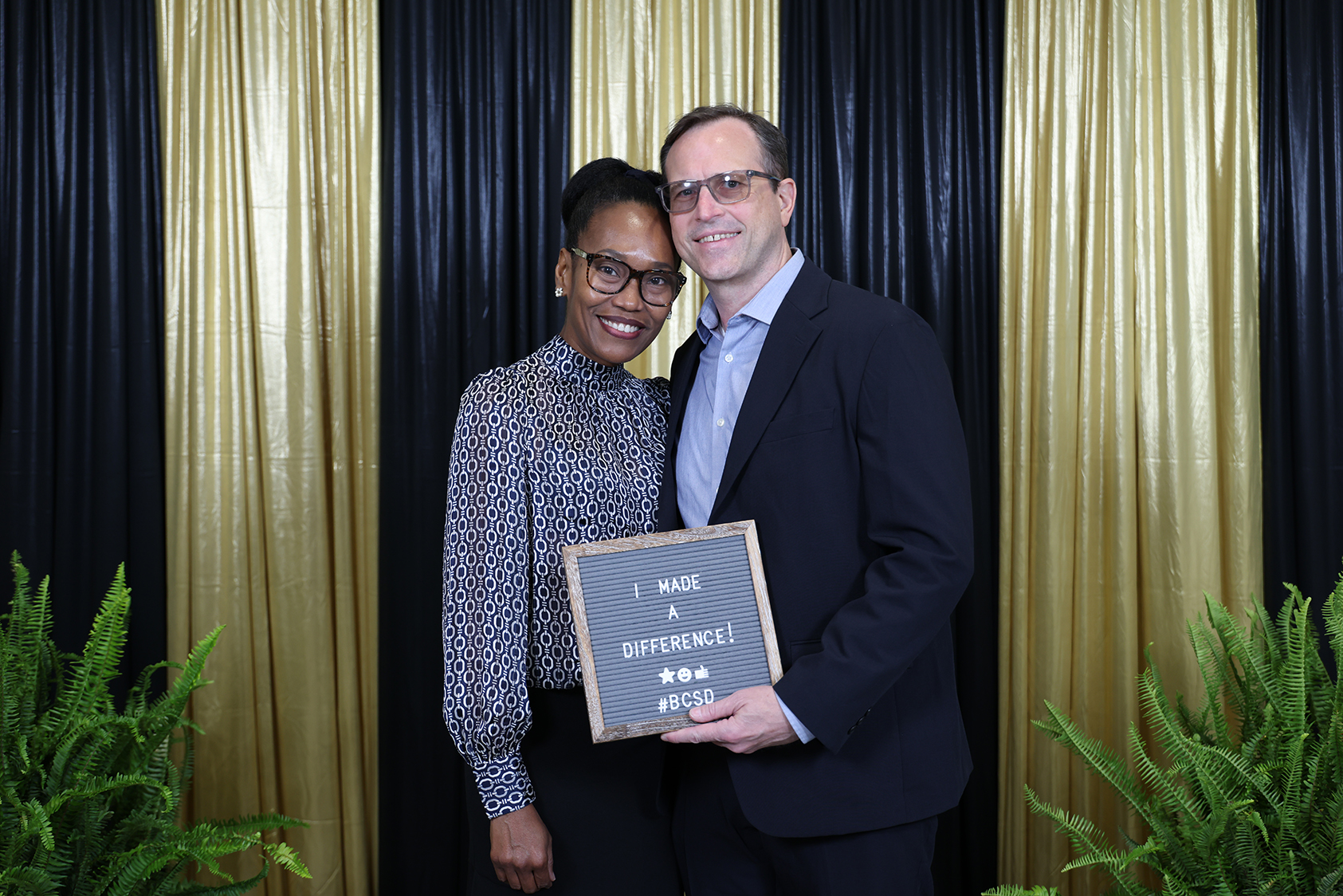 A man and a woman stand together holding a framed plaque with the words "I made a difference".